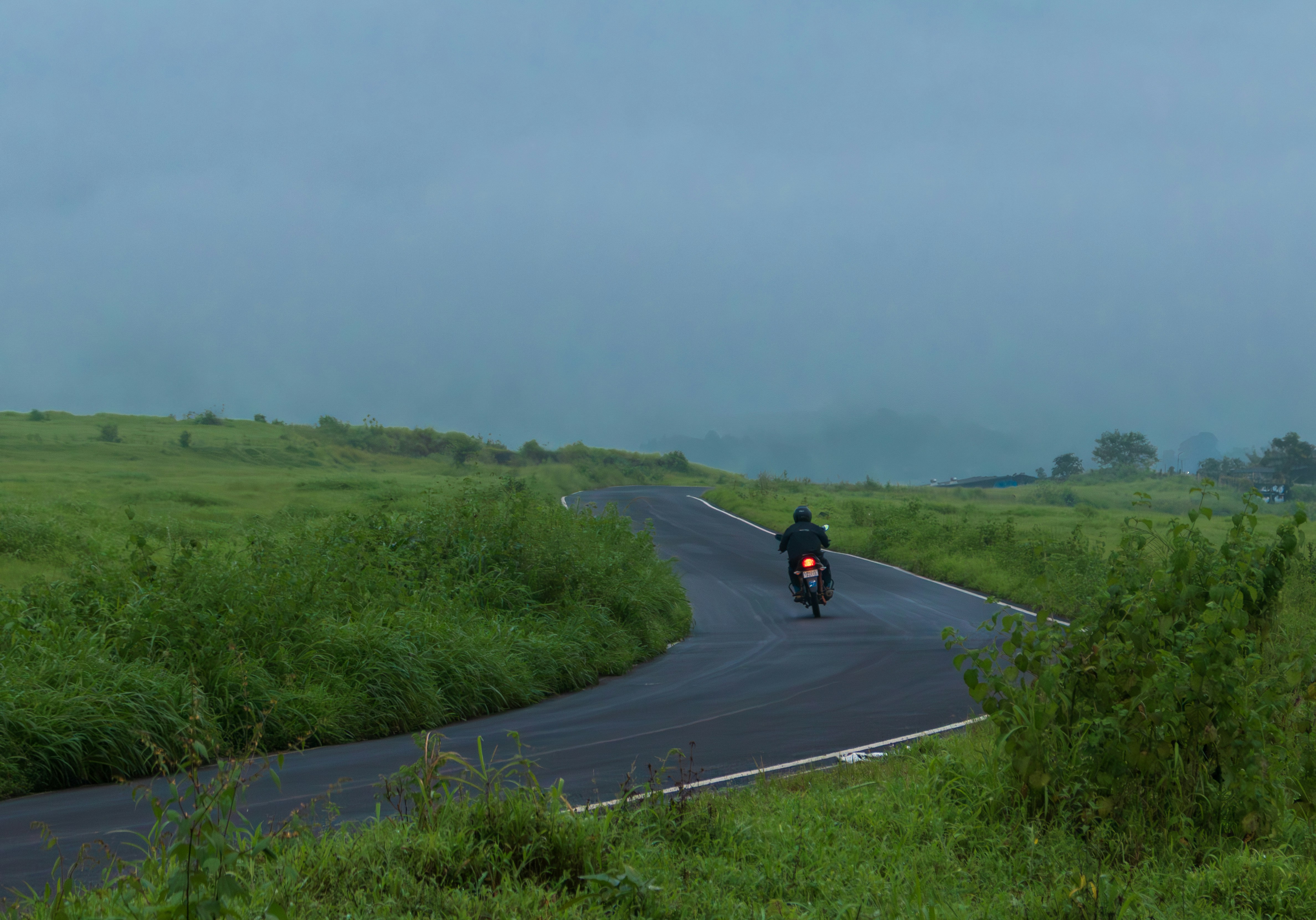 Motorcyclist on a winding road through grassy hills