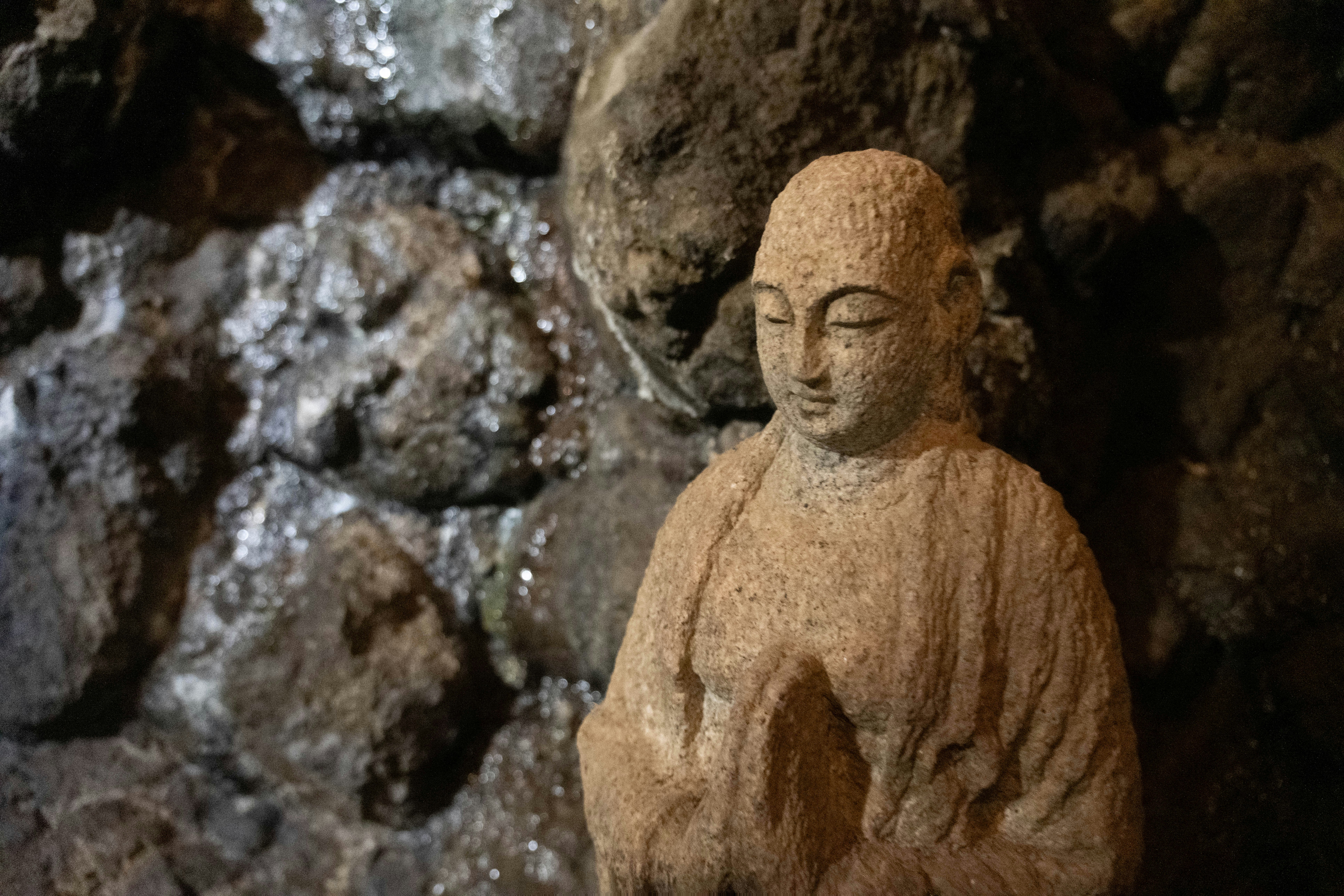 Stone statue of buddha with hands clasped in prayer.