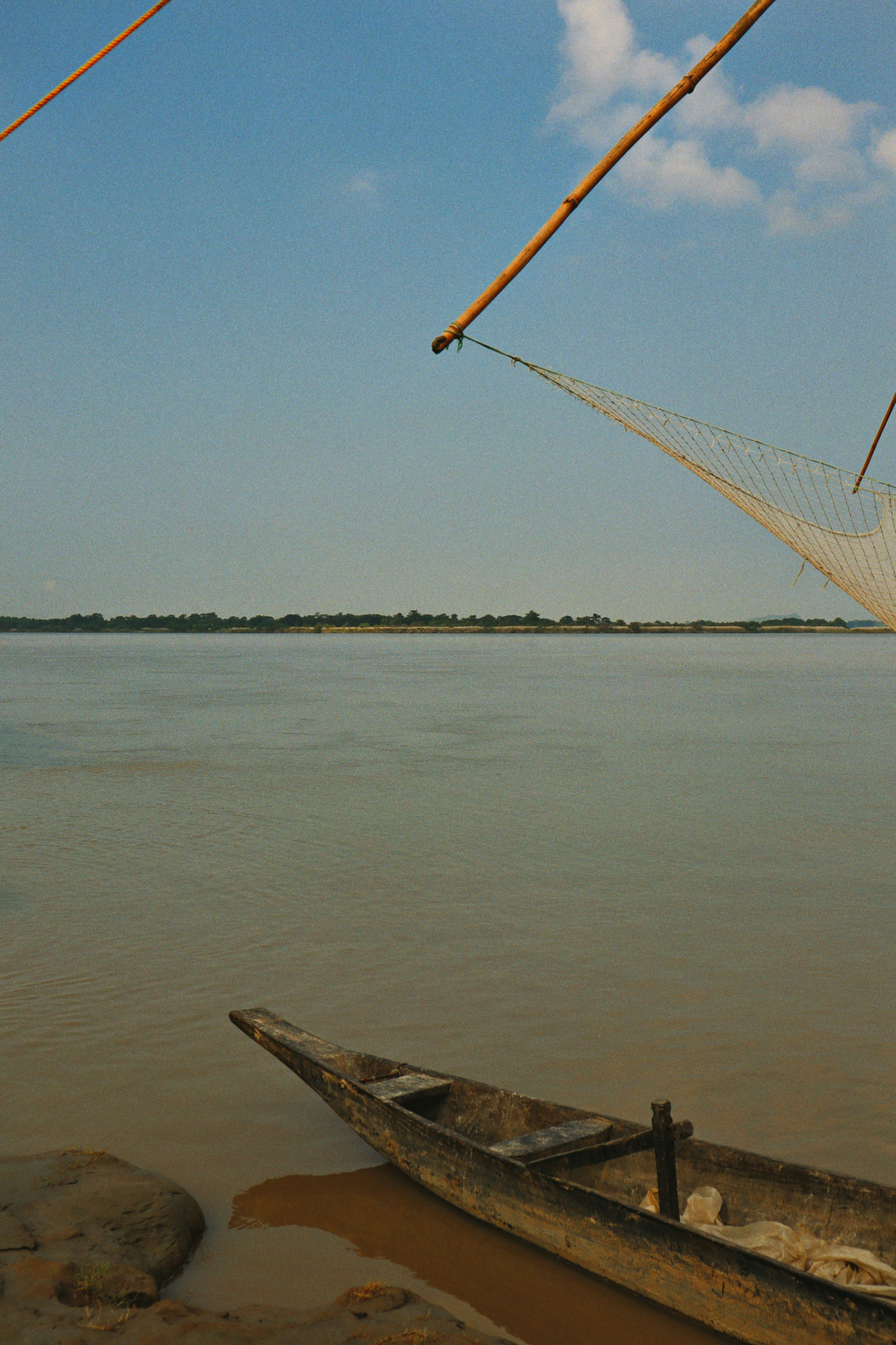 A wooden canoe rests by a wide, calm river.