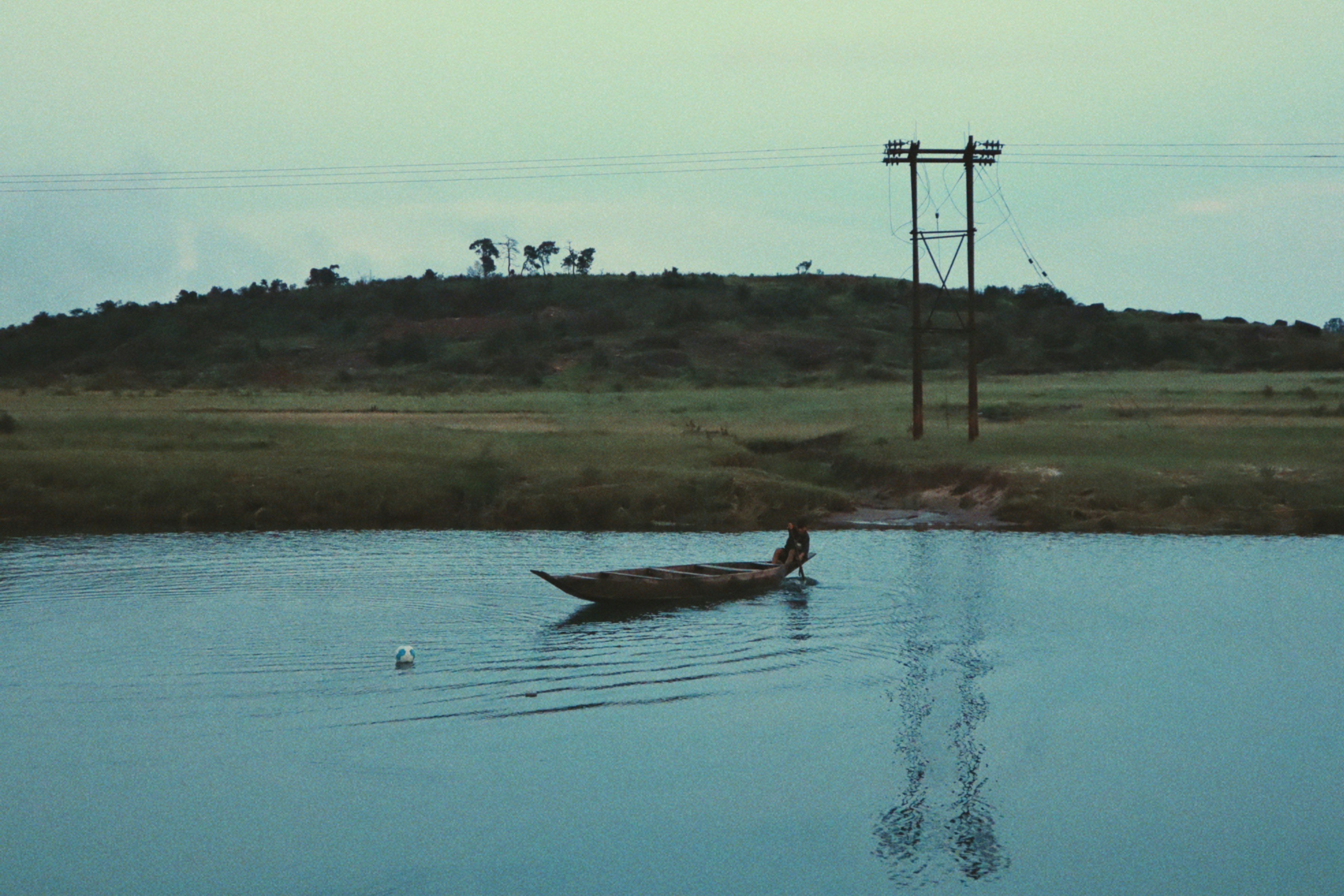 A lone person rows a boat on a calm river.