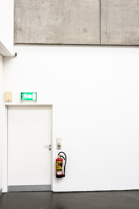Fire extinguisher next to green exit sign on white wall - fire safety and emergency signage in a building