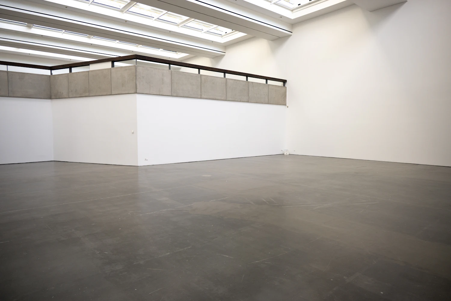 An empty gallery with a polished concrete floor lit from above