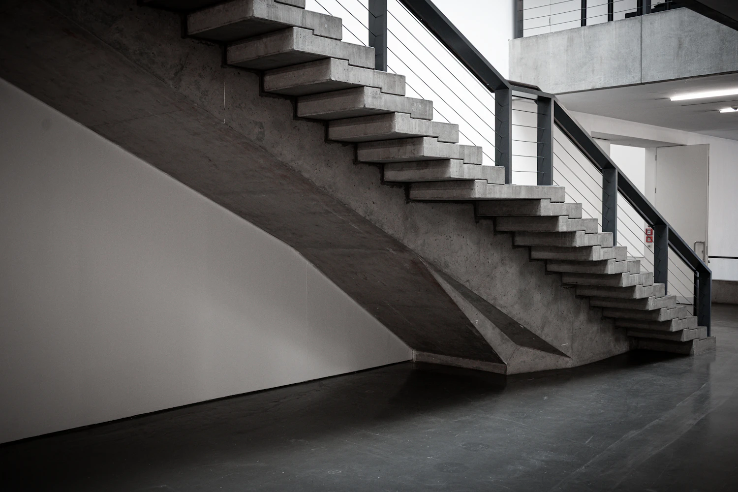 A board-marked concrete stair rising past a white wall
