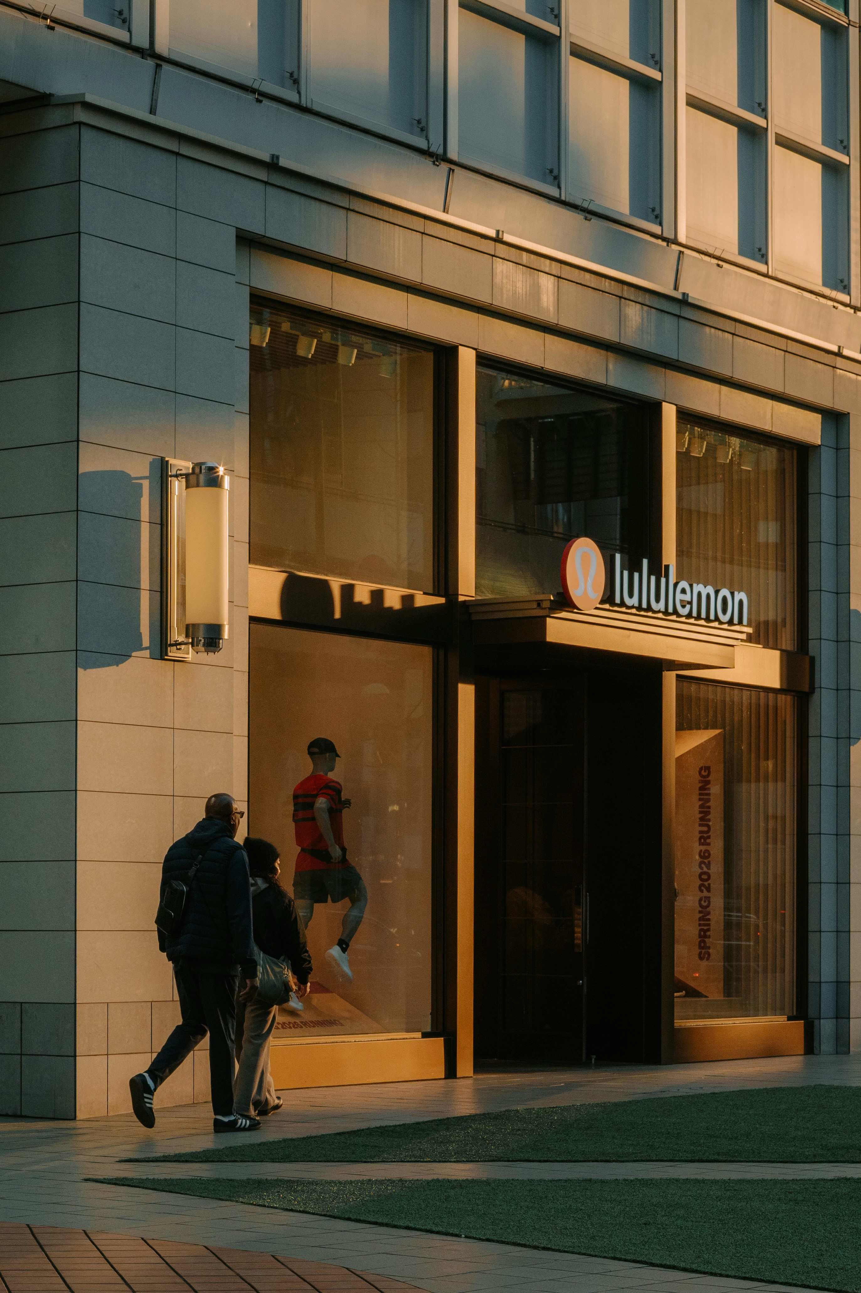 People walk past a lululemon store at sunset.
