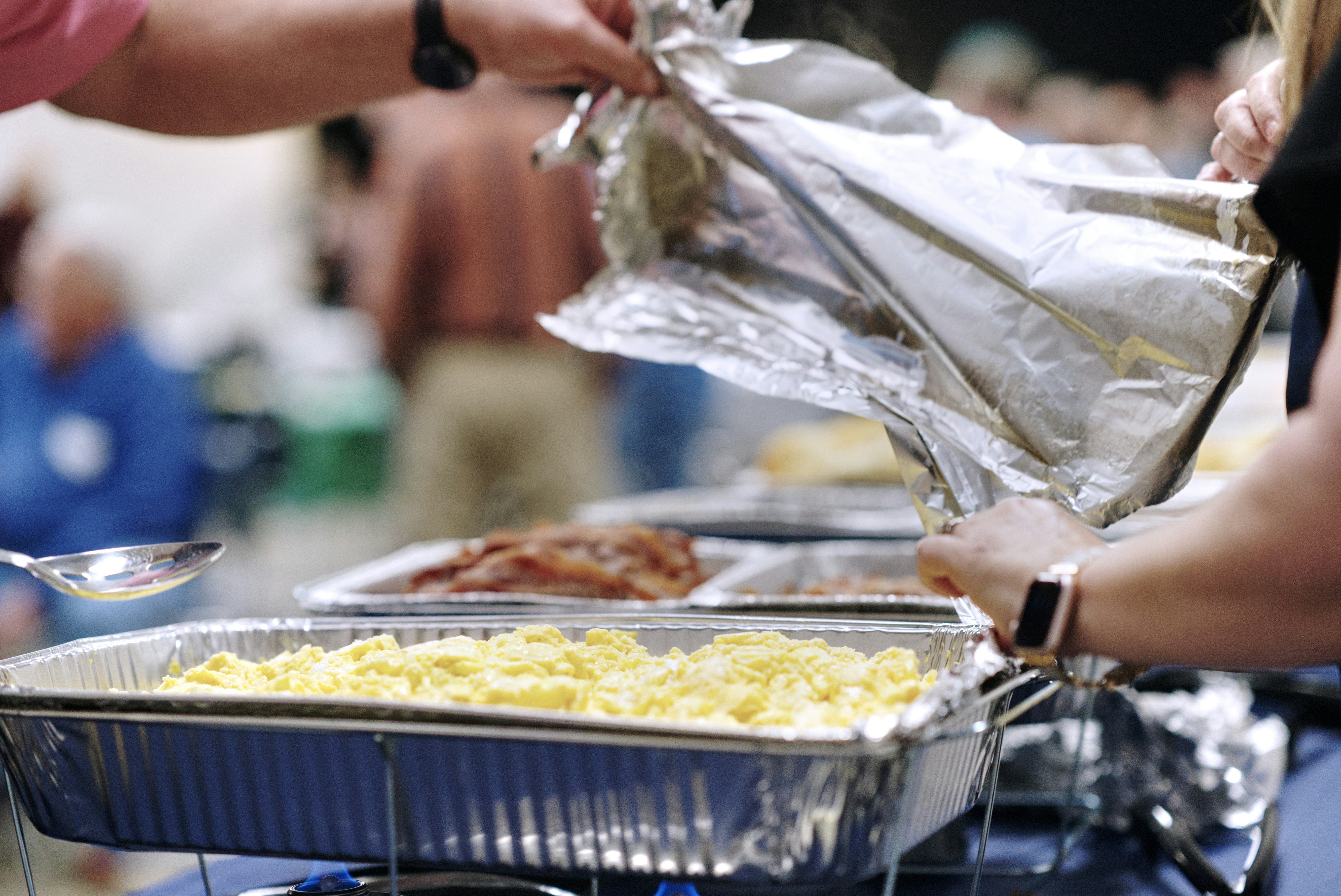 A tray of scrambled eggs being uncovered ready for serving in a buffet breakfast line