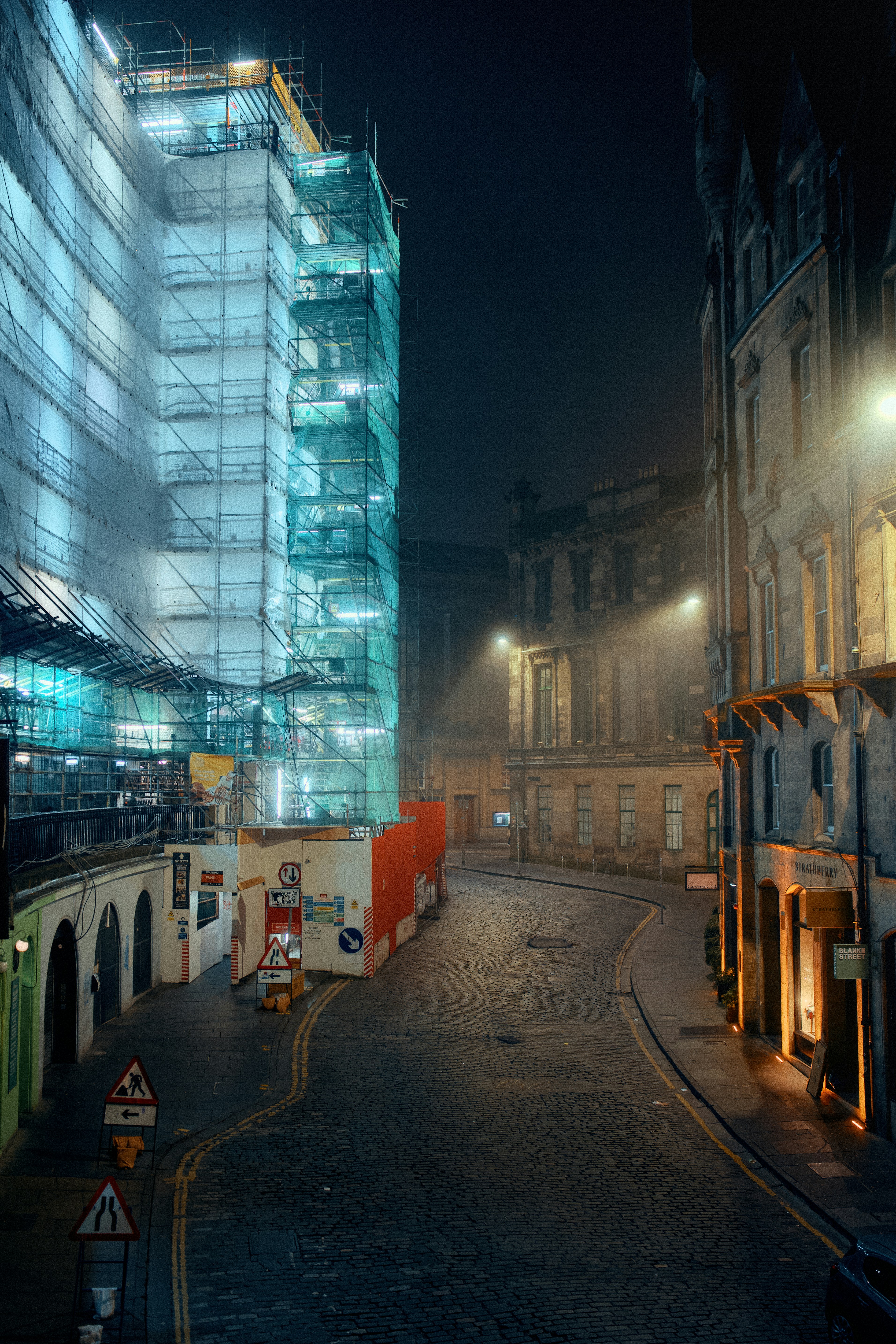 Scaffolding covers building under construction at night.