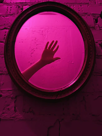 Hand reaching out in a pink illuminated mirror