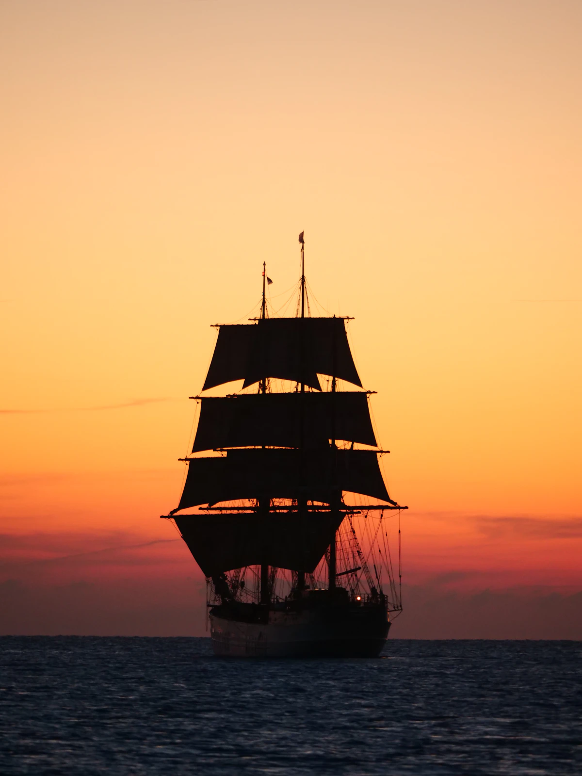 A tall ship sailing on the ocean at sunset