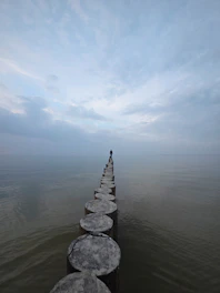 Lone figure stands on wooden posts over water