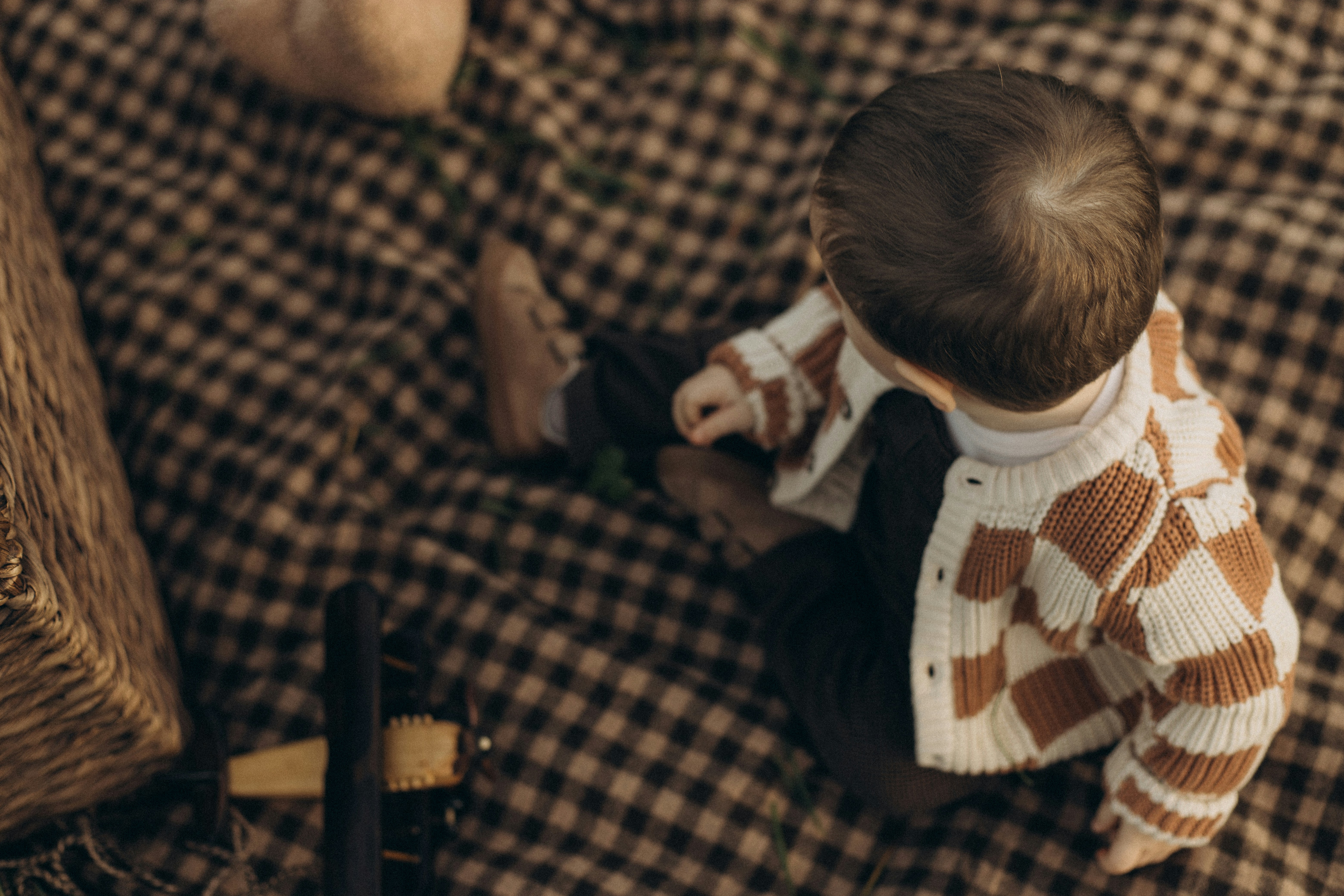 A baby sits on a checkered blanket with a basket.