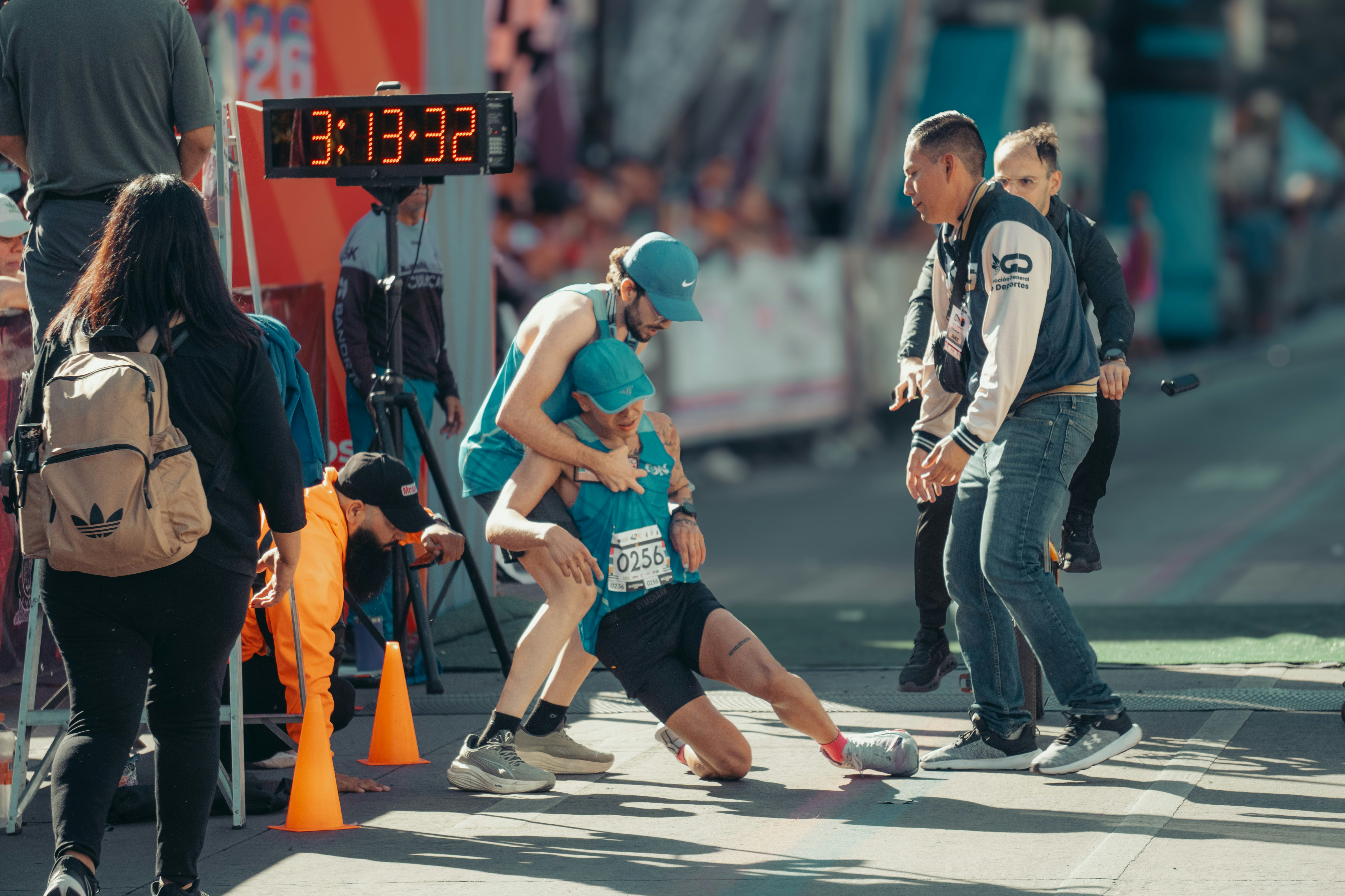 Runner collapses at finish line, helped by others.