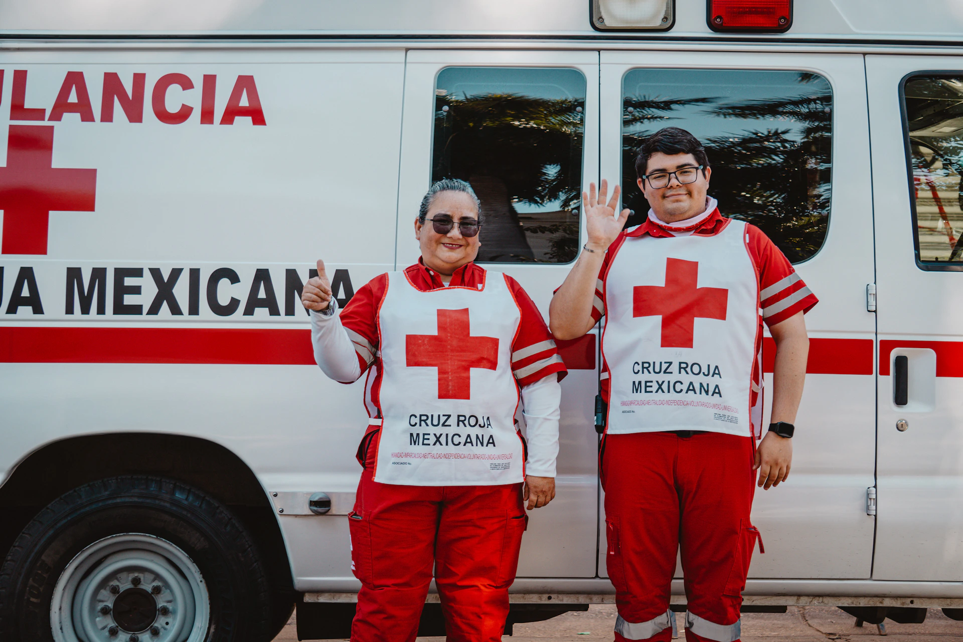 Two people in cruz roja mexicana uniforms waving.