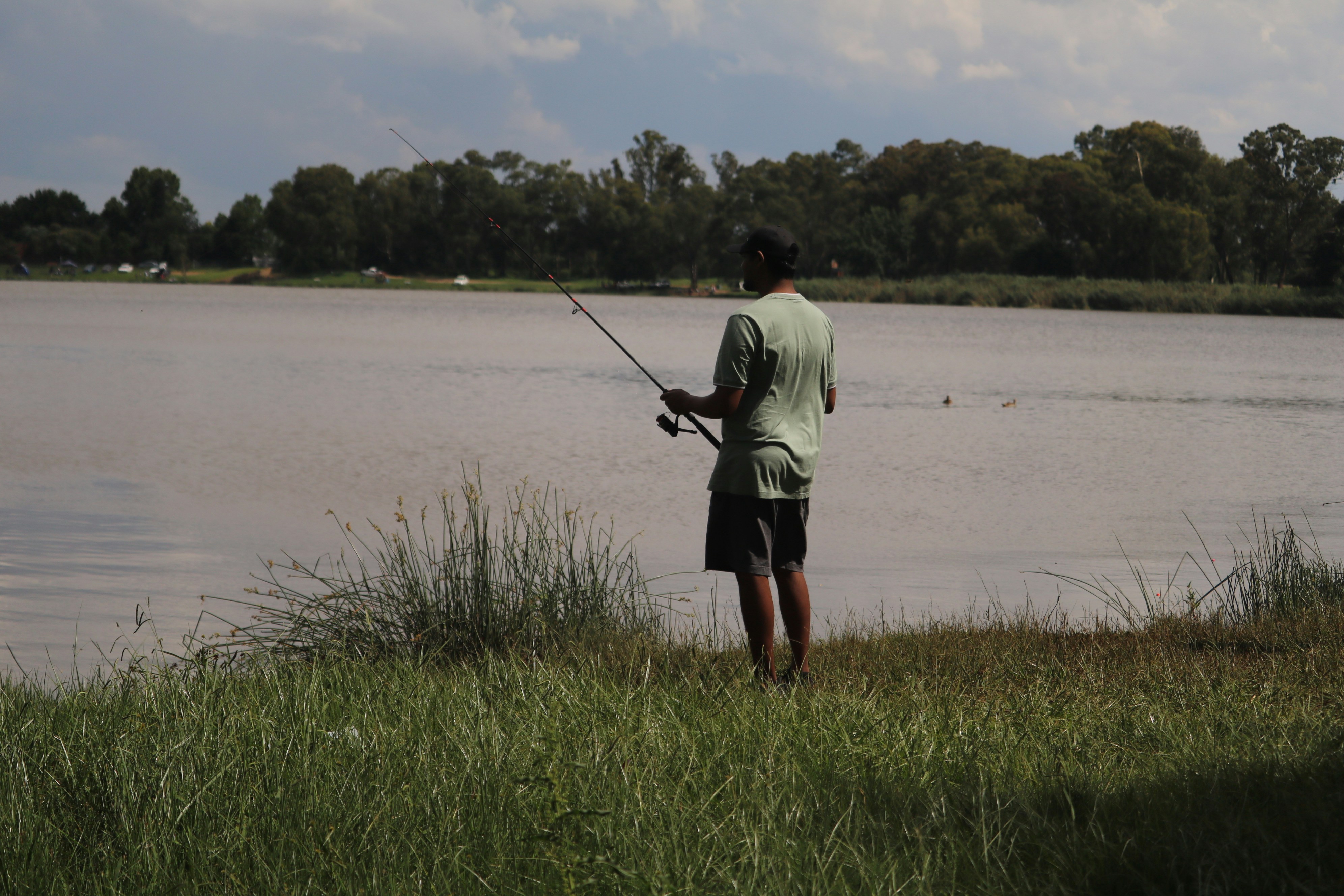 Man fishing by the calm lake shore
