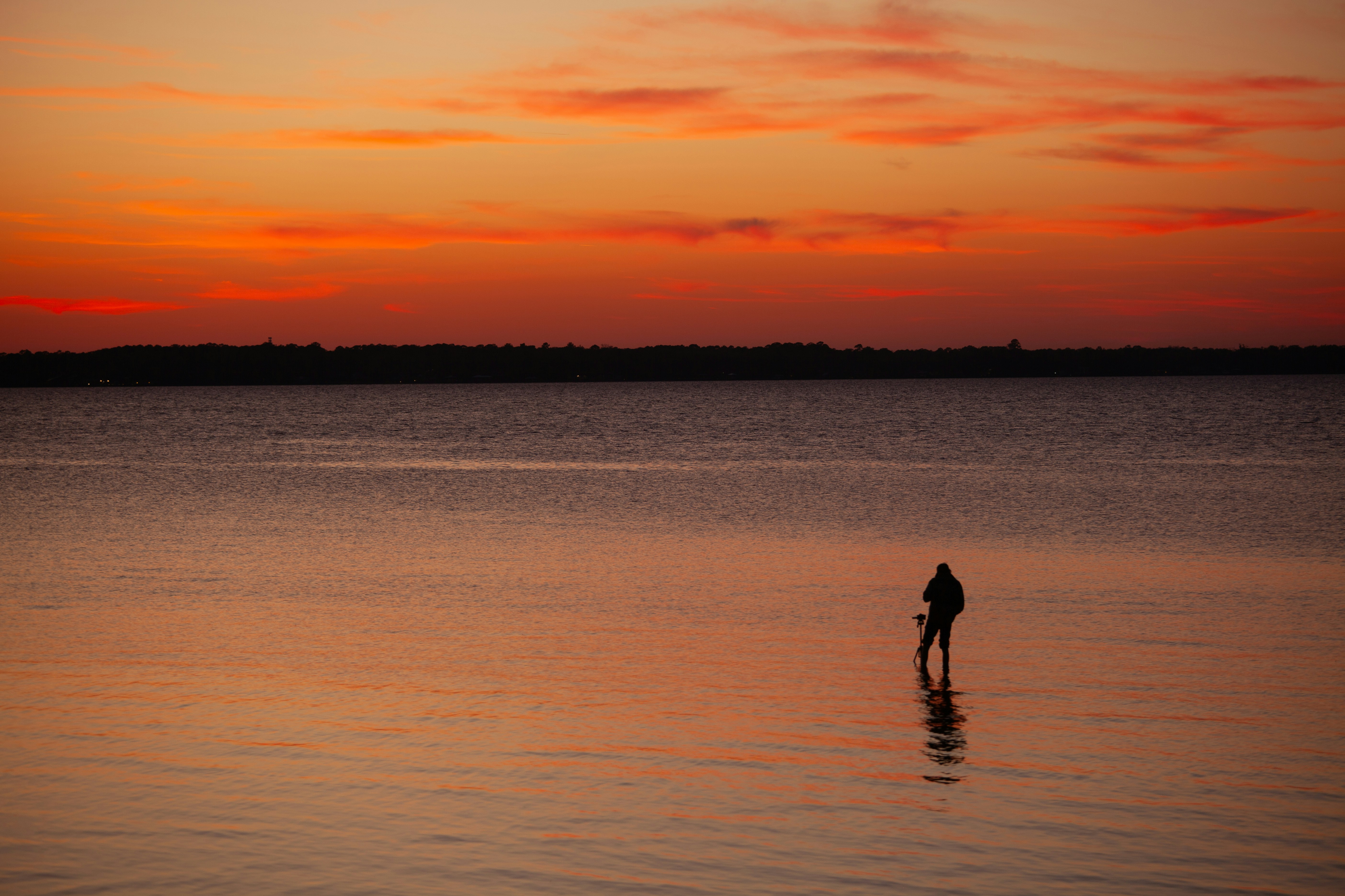 Una figura solitaria está de pie sobre el agua tranquila al atardecer.