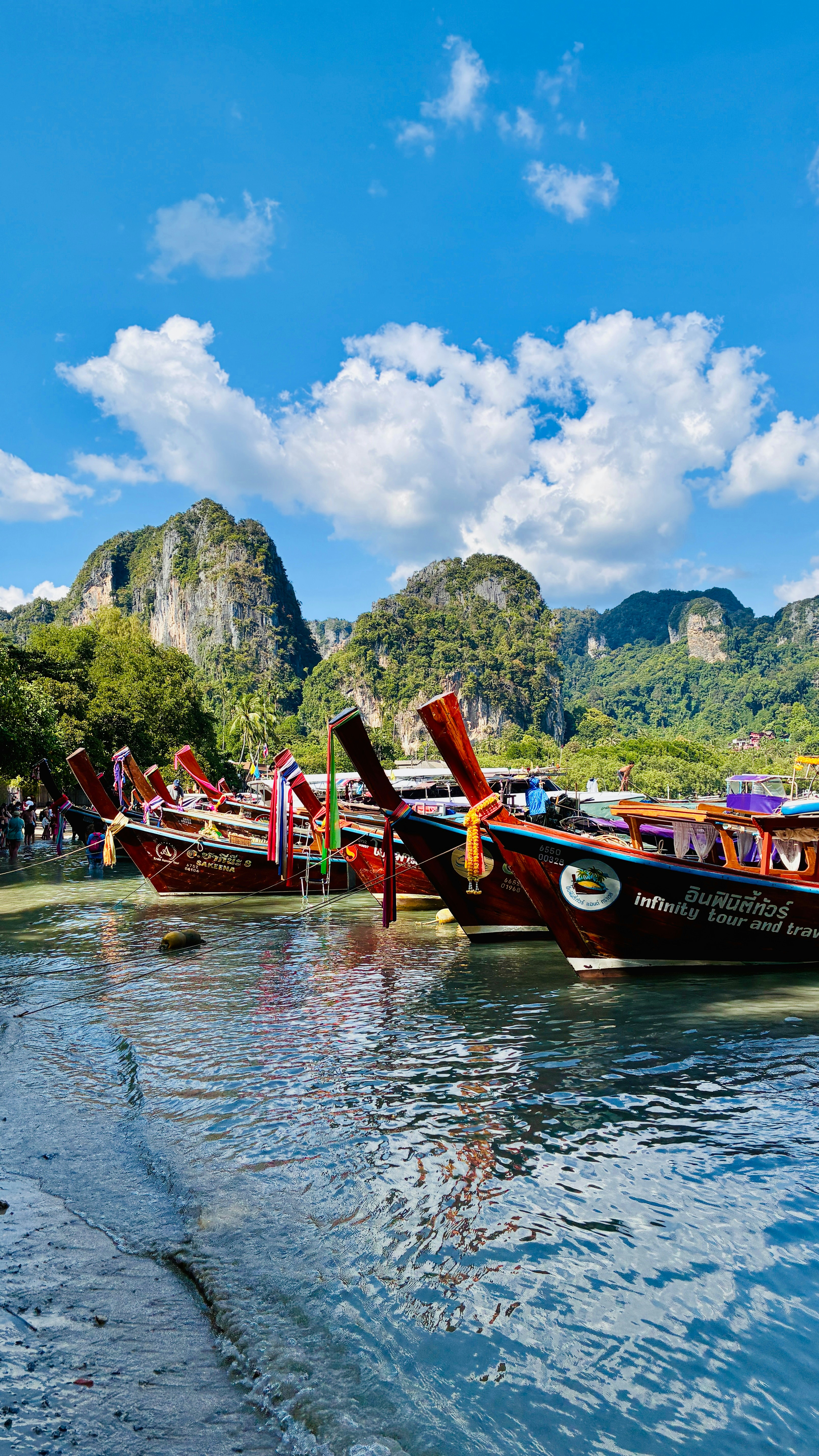 Longtail boats docked by limestone cliffs under a blue sky.