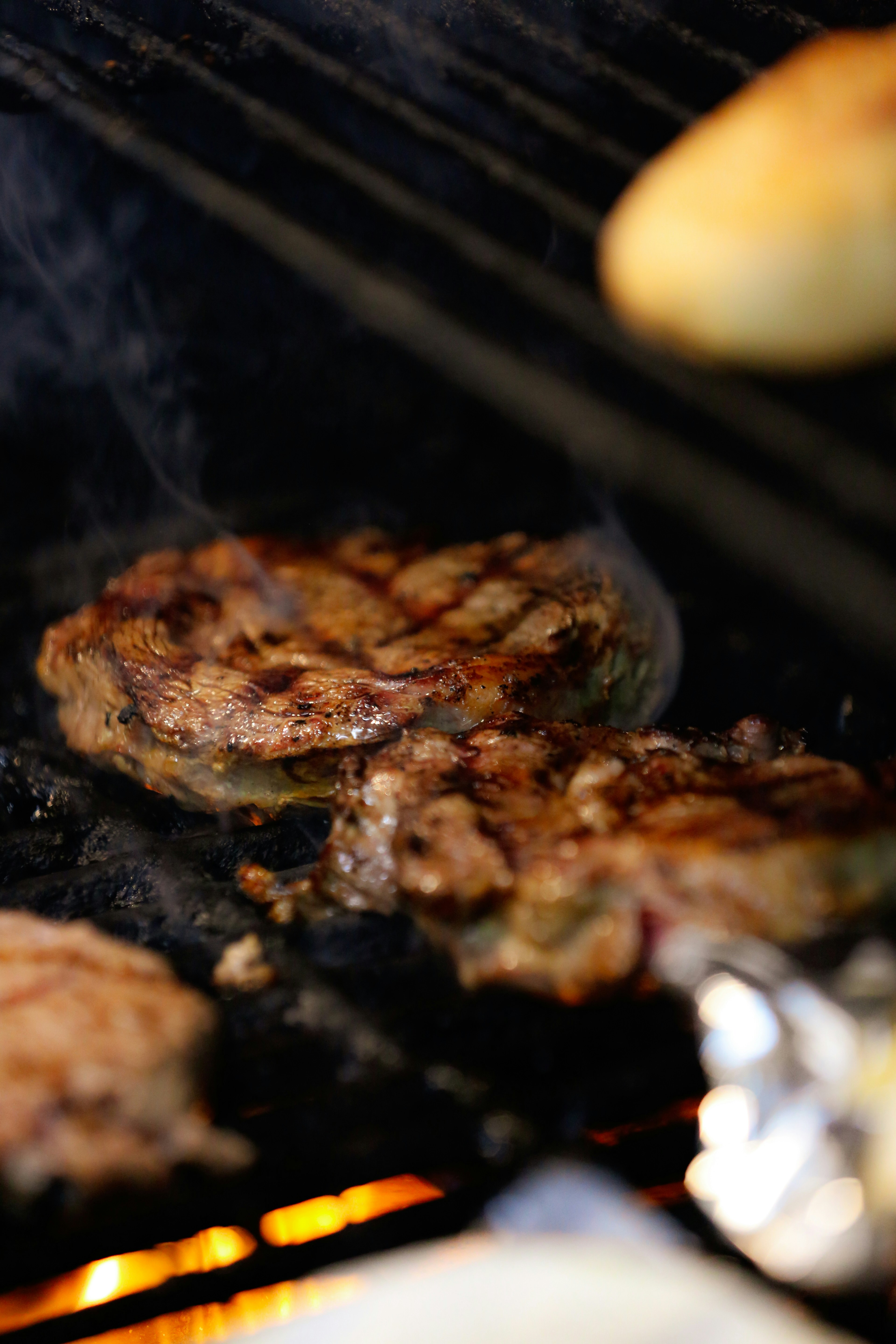 Steaks cooking on a hot grill with flames below.