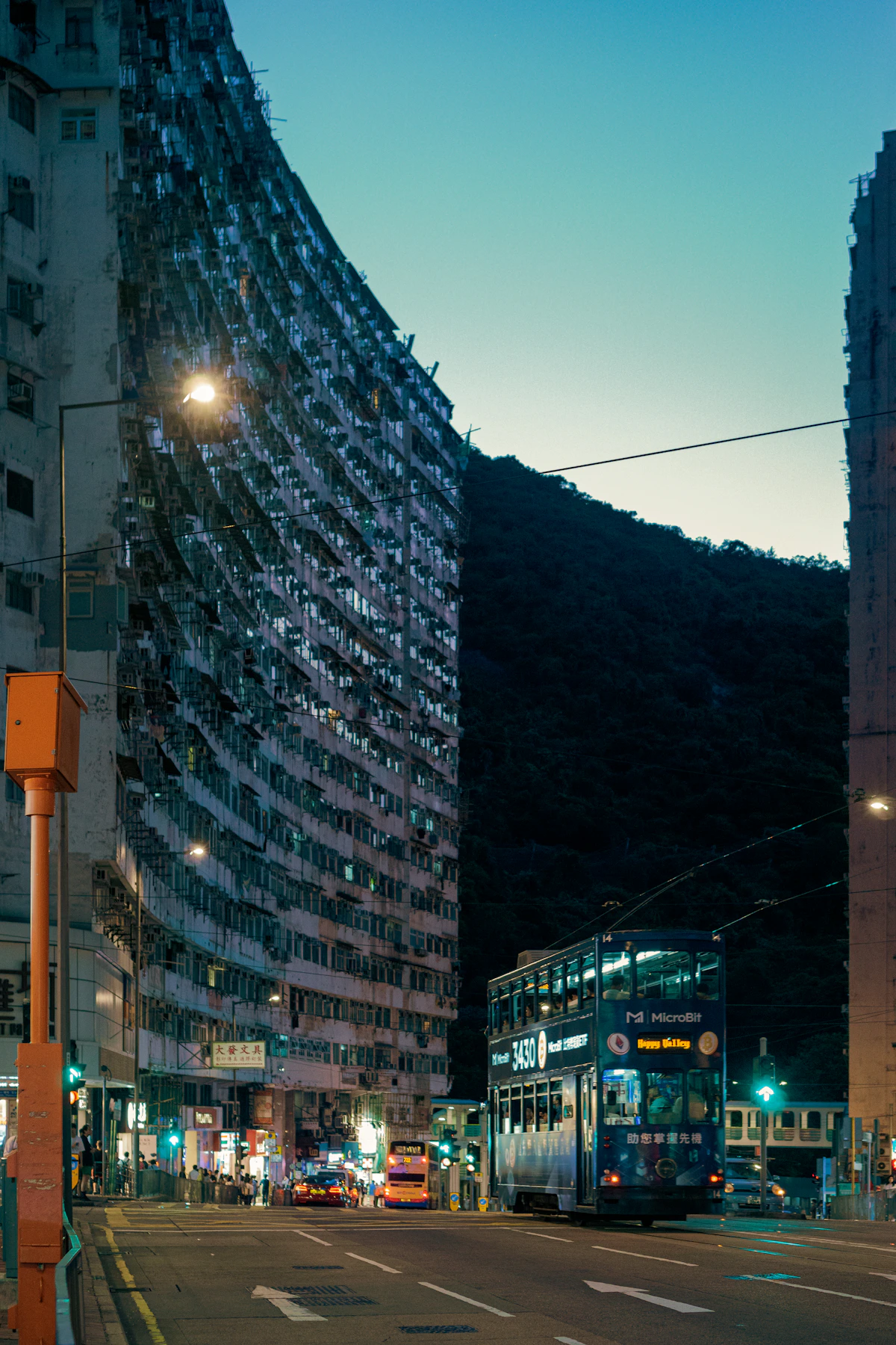 A blue double-decker tram passing dense apartment buildings in Quarry Bay at dusk