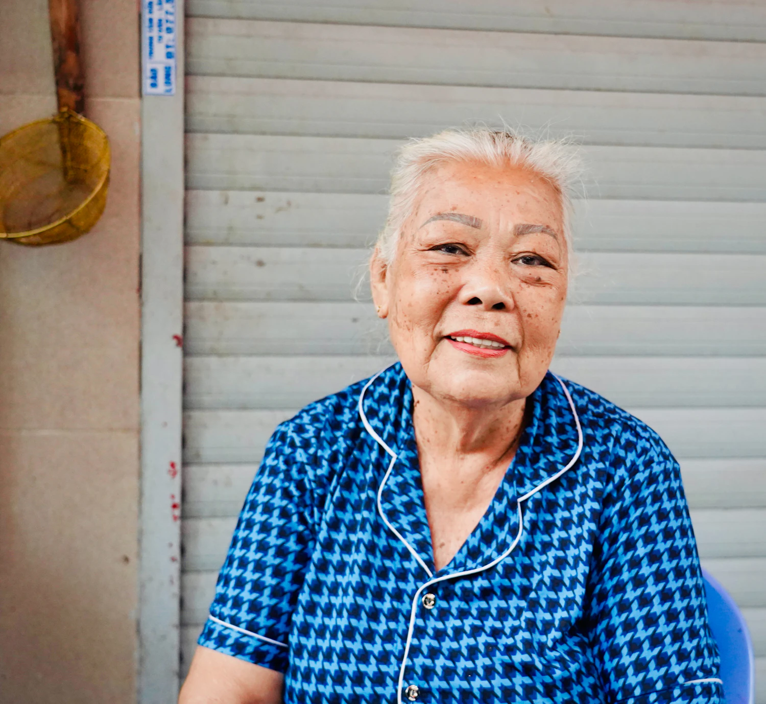 An older woman with white hair in a blue patterned shirt, smiling in a doorway