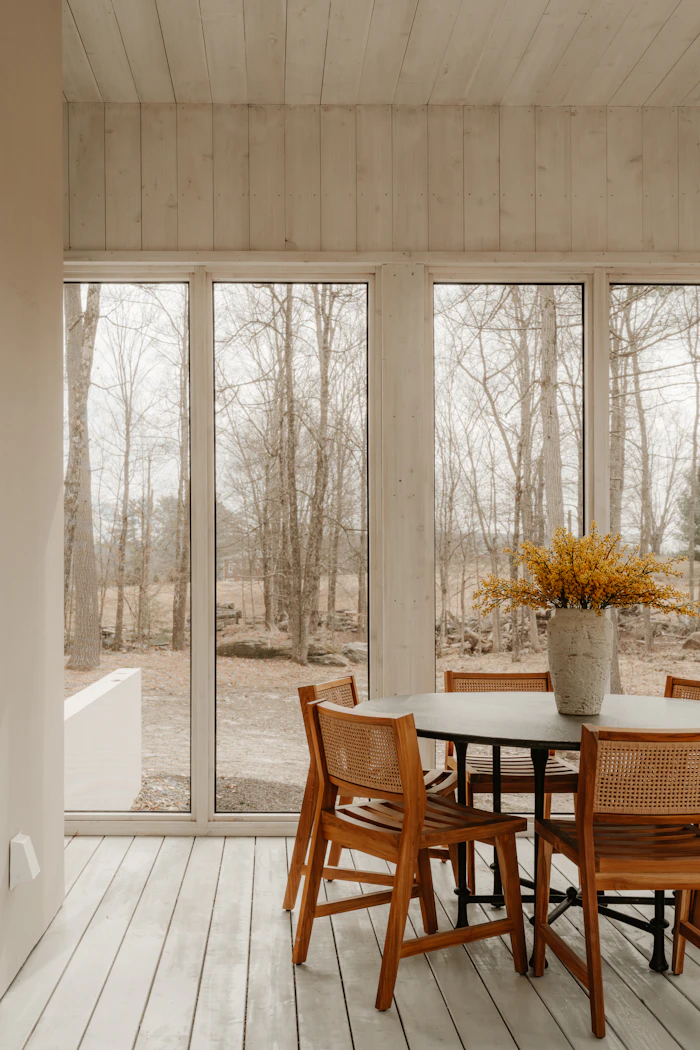 Dining chairs set against a window wall of trees