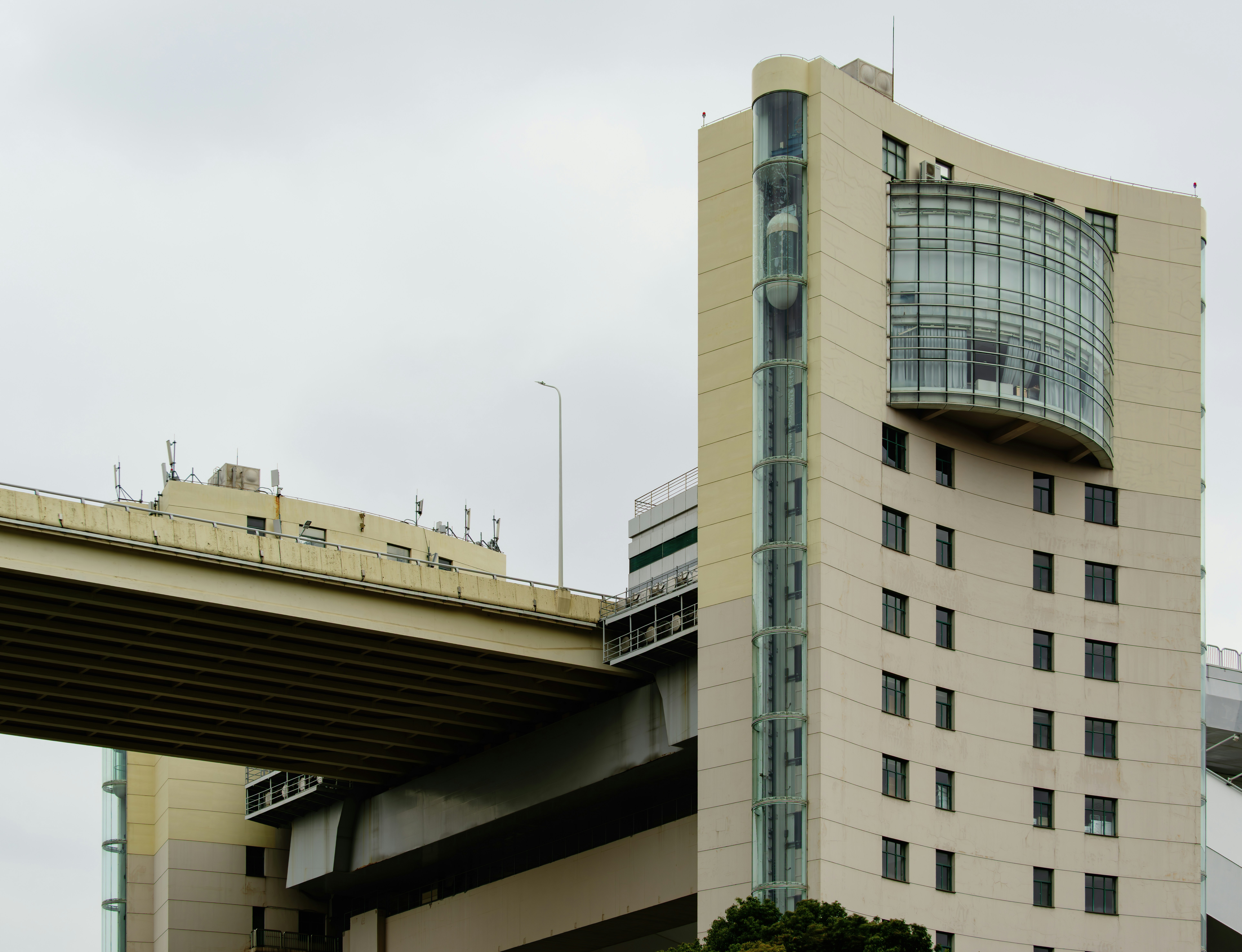 Modern building with curved glass section and elevated roadway.