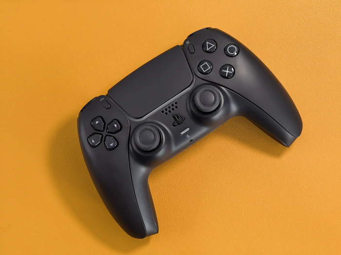 Black wireless game controller on an orange background
