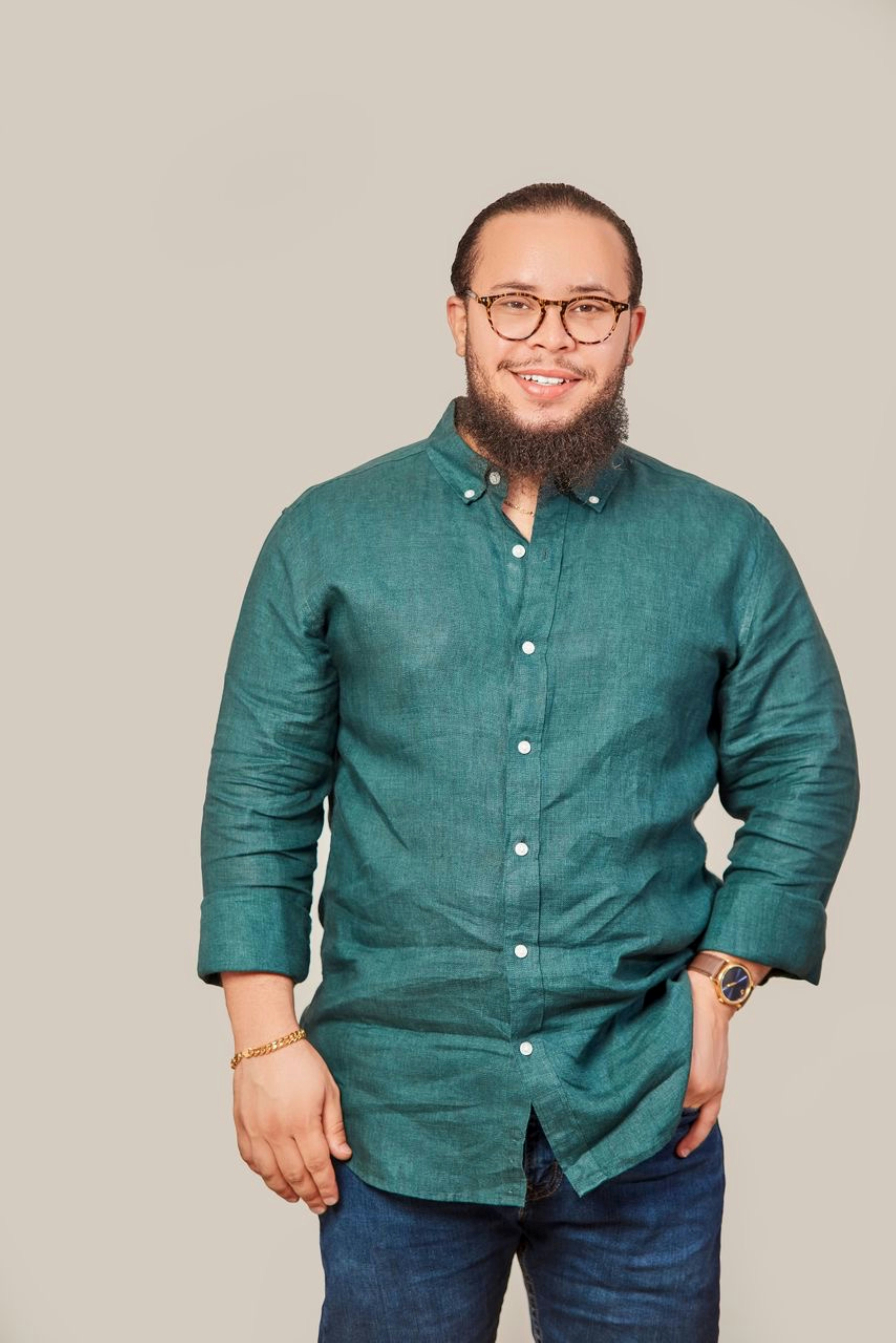Um homem sorridente, com barba, óculos e camisa verde