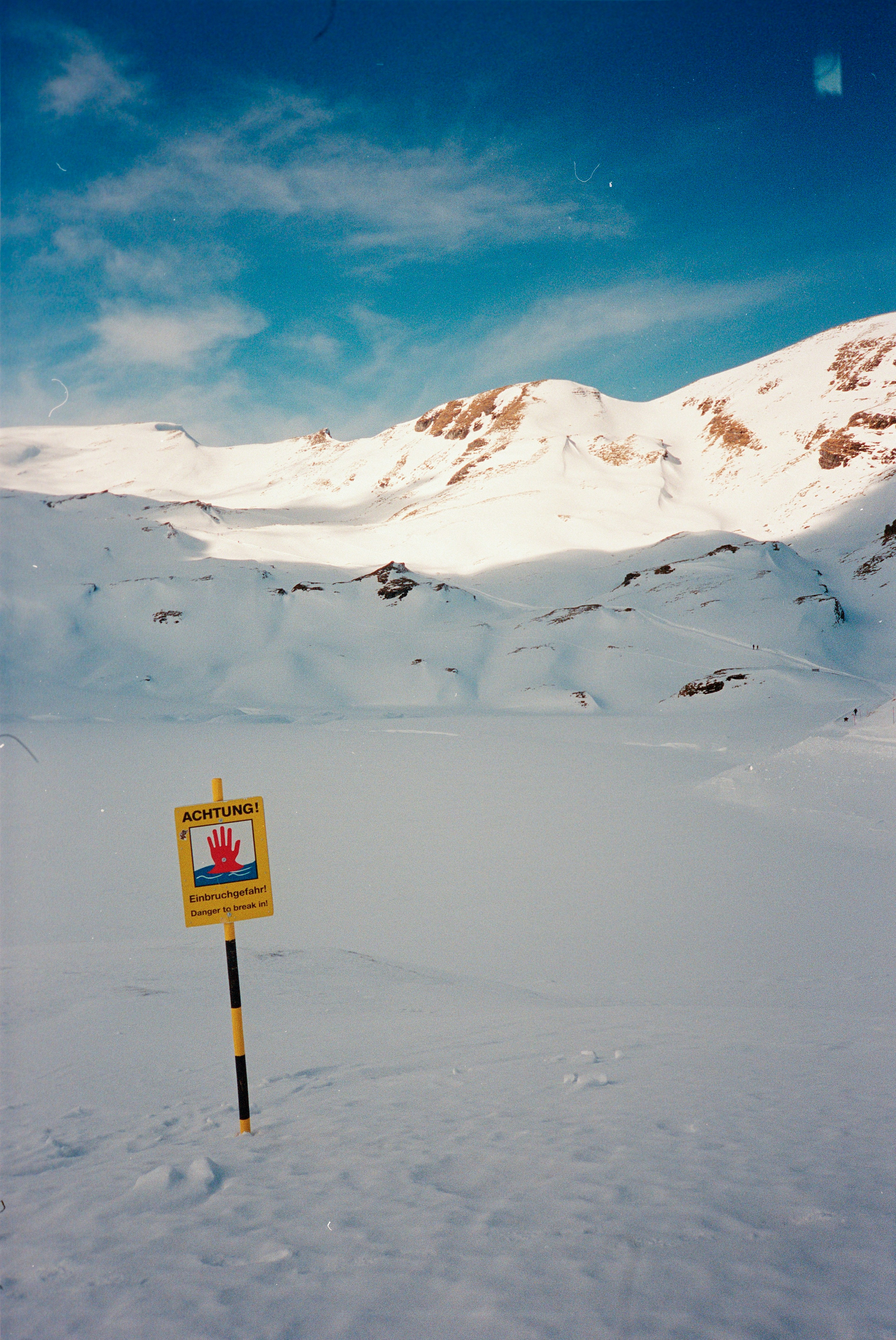 Yellow warning sign in a snowy mountain landscape.