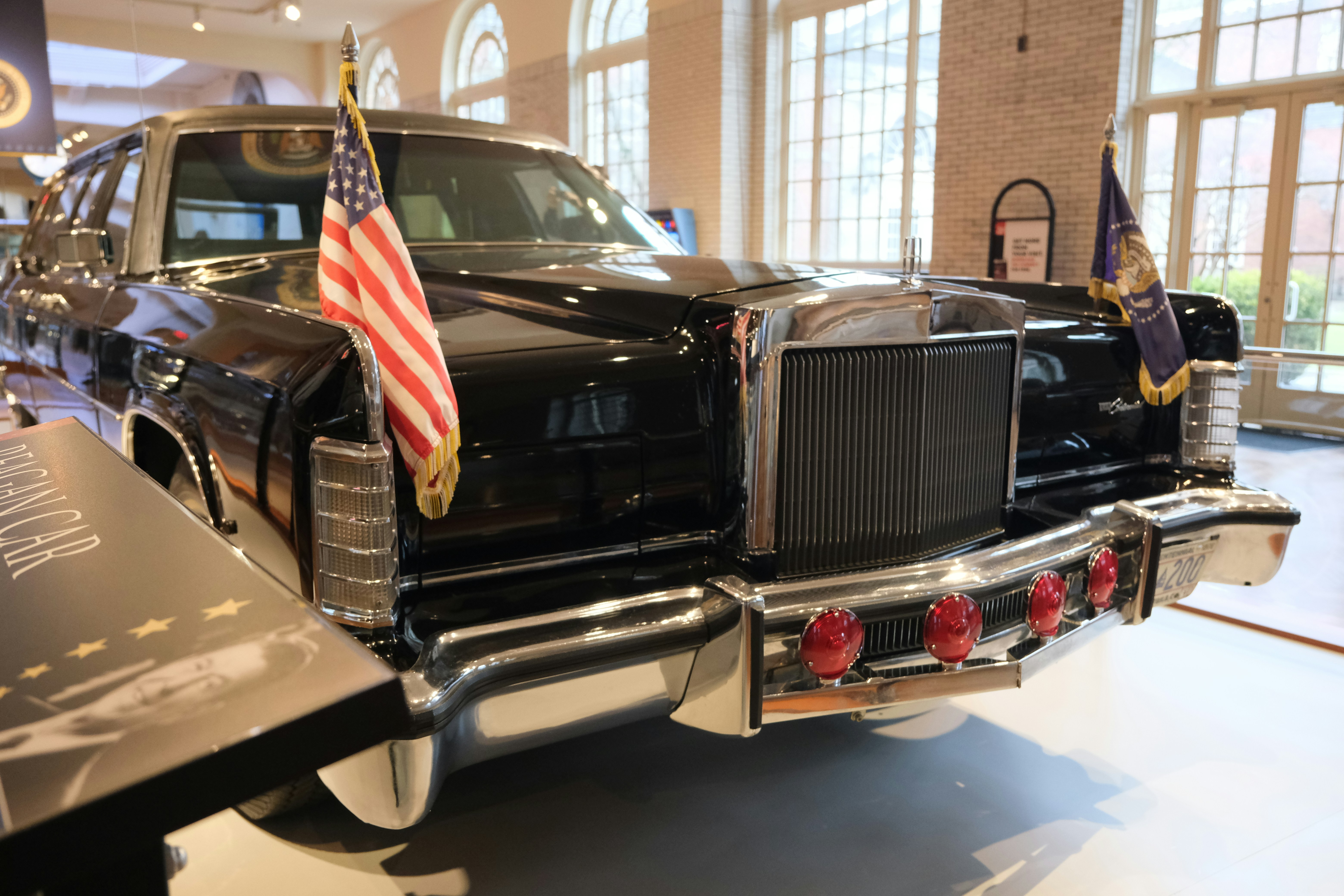 A black presidential limousine with flags on front.