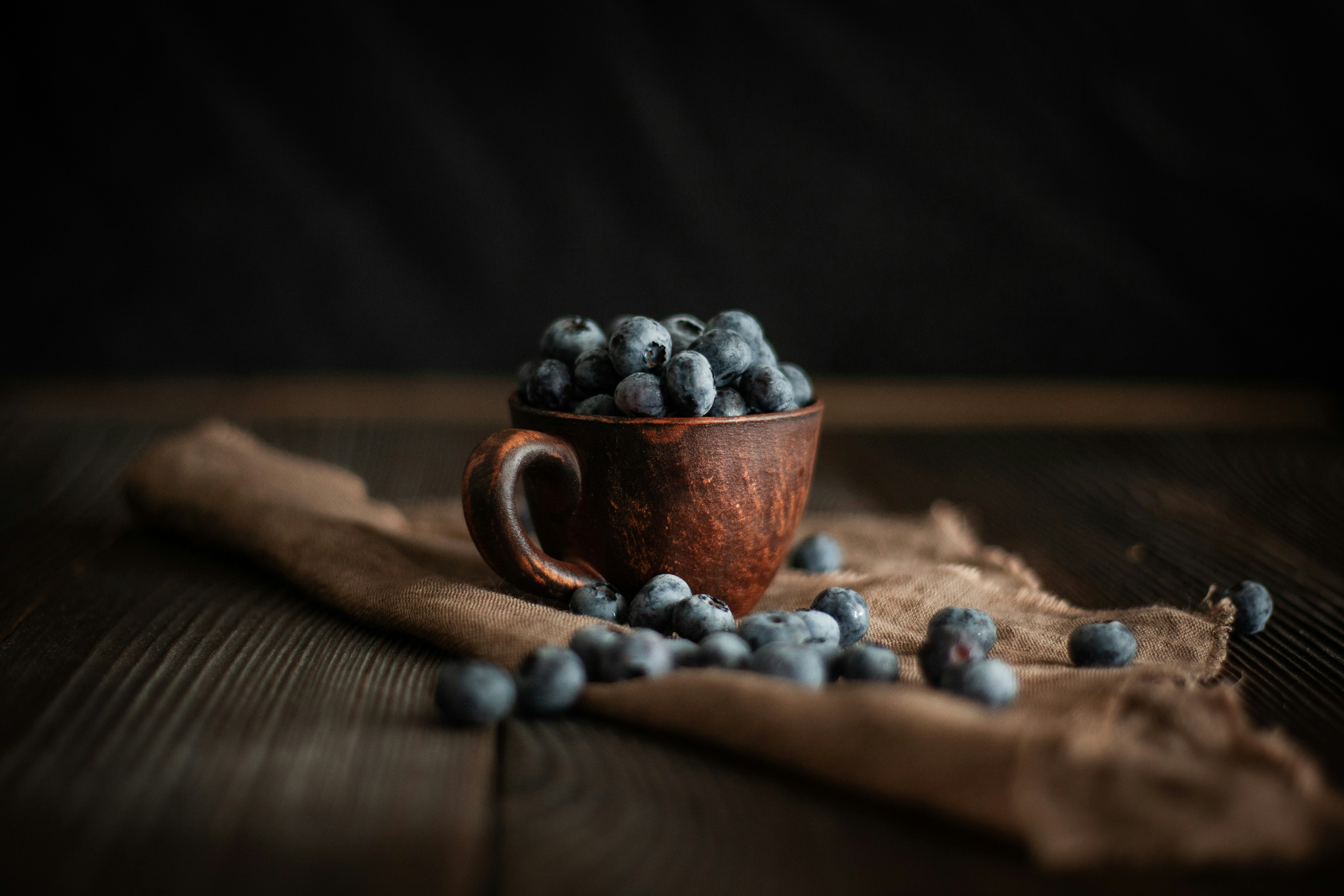 A rustic wooden cup filled with fresh blueberries