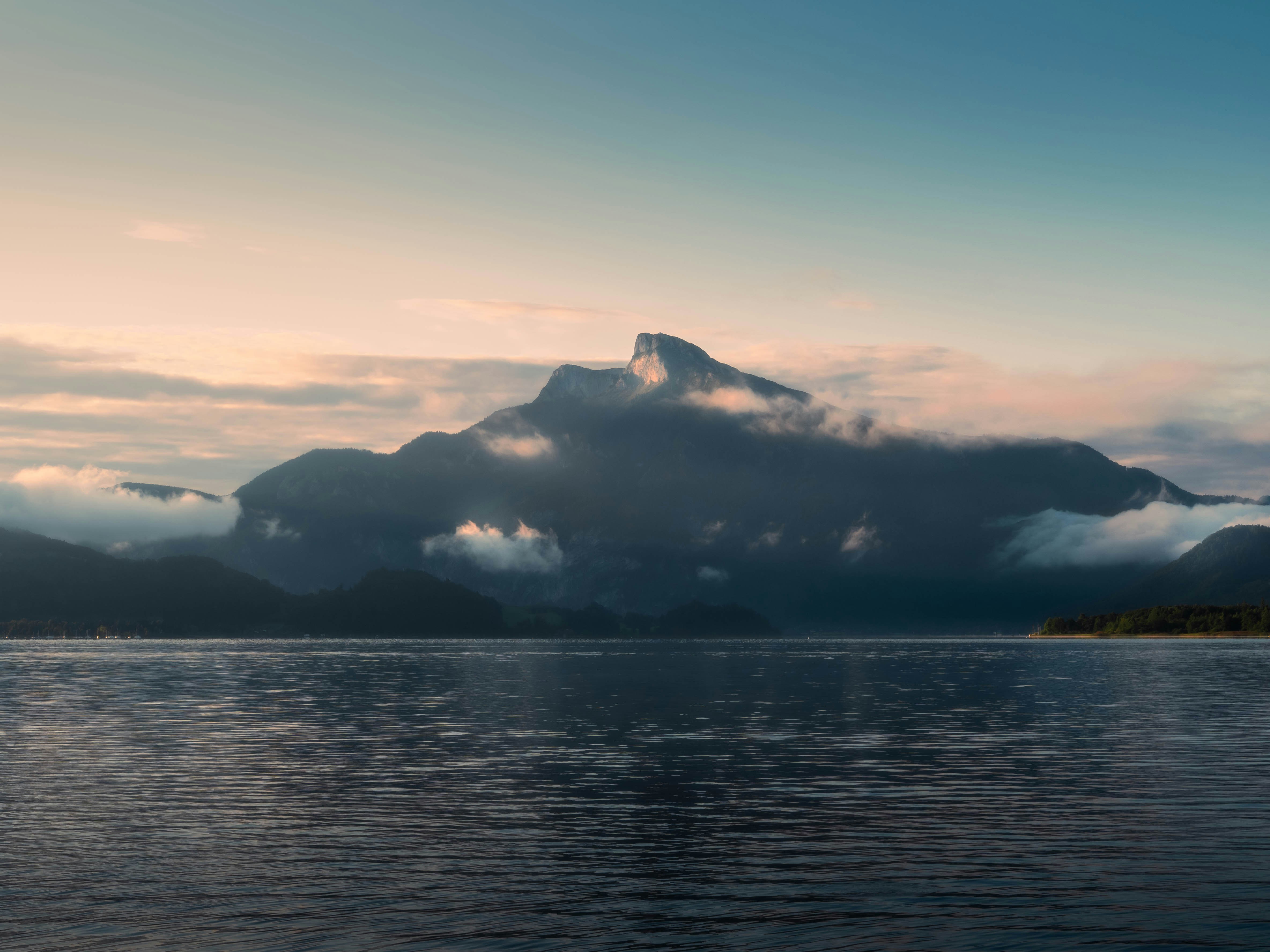 霧のかかった山々が夜明けに穏やかな湖の上にそびえ立っています。