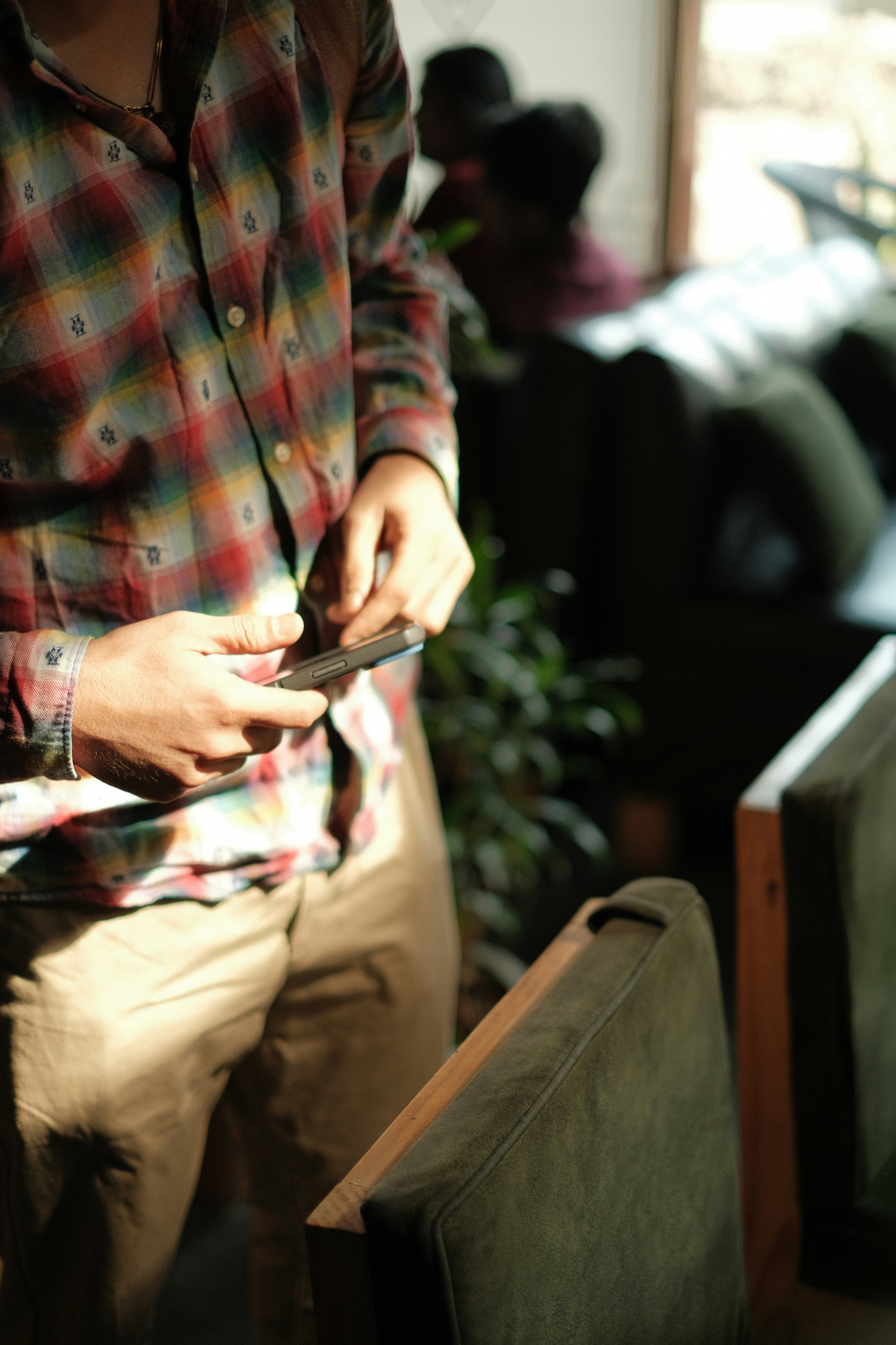 Uomo con camicia a quadri che tiene uno smartphone al chiuso