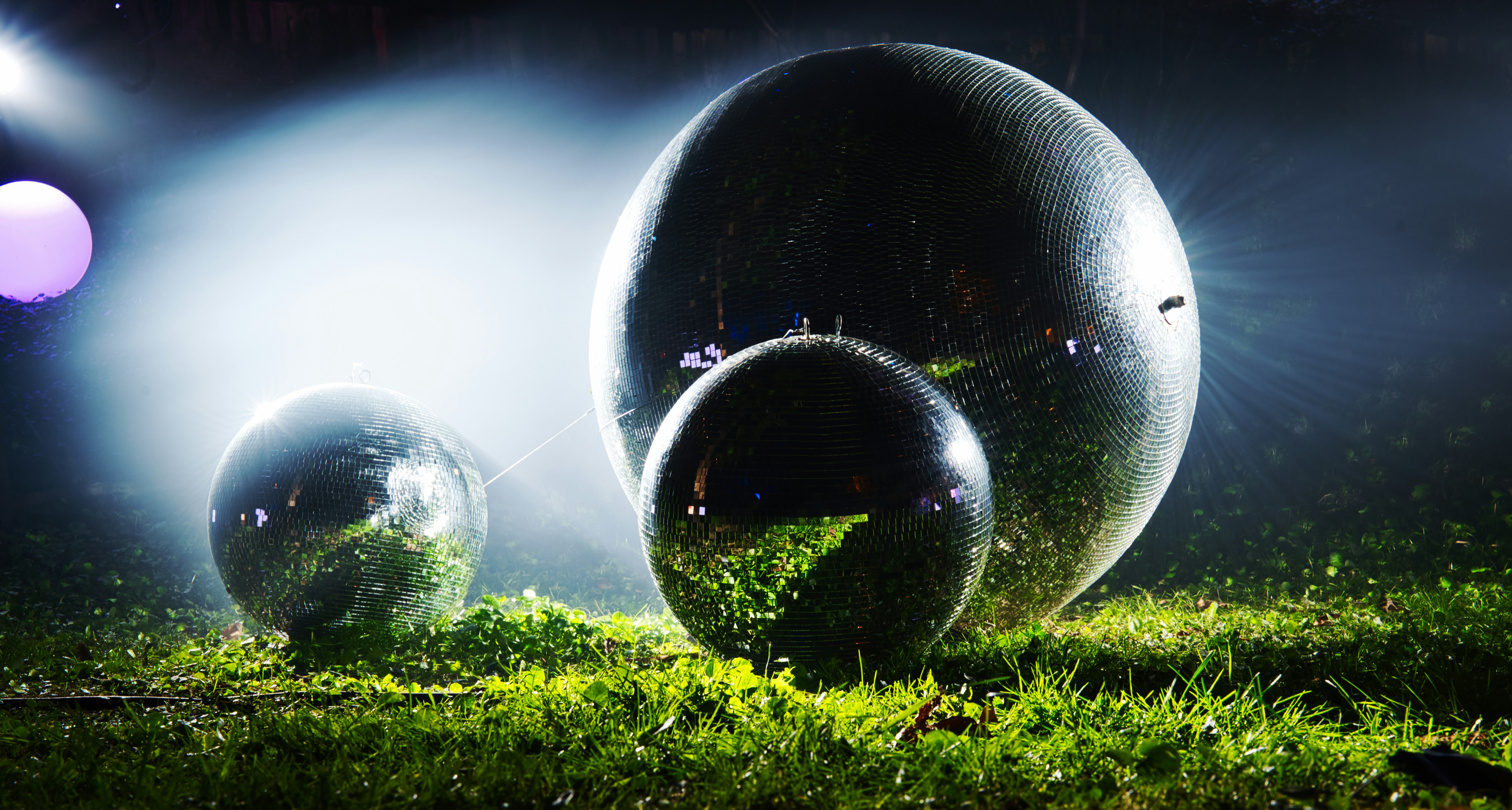 Three reflective spheres on grassy ground at night.