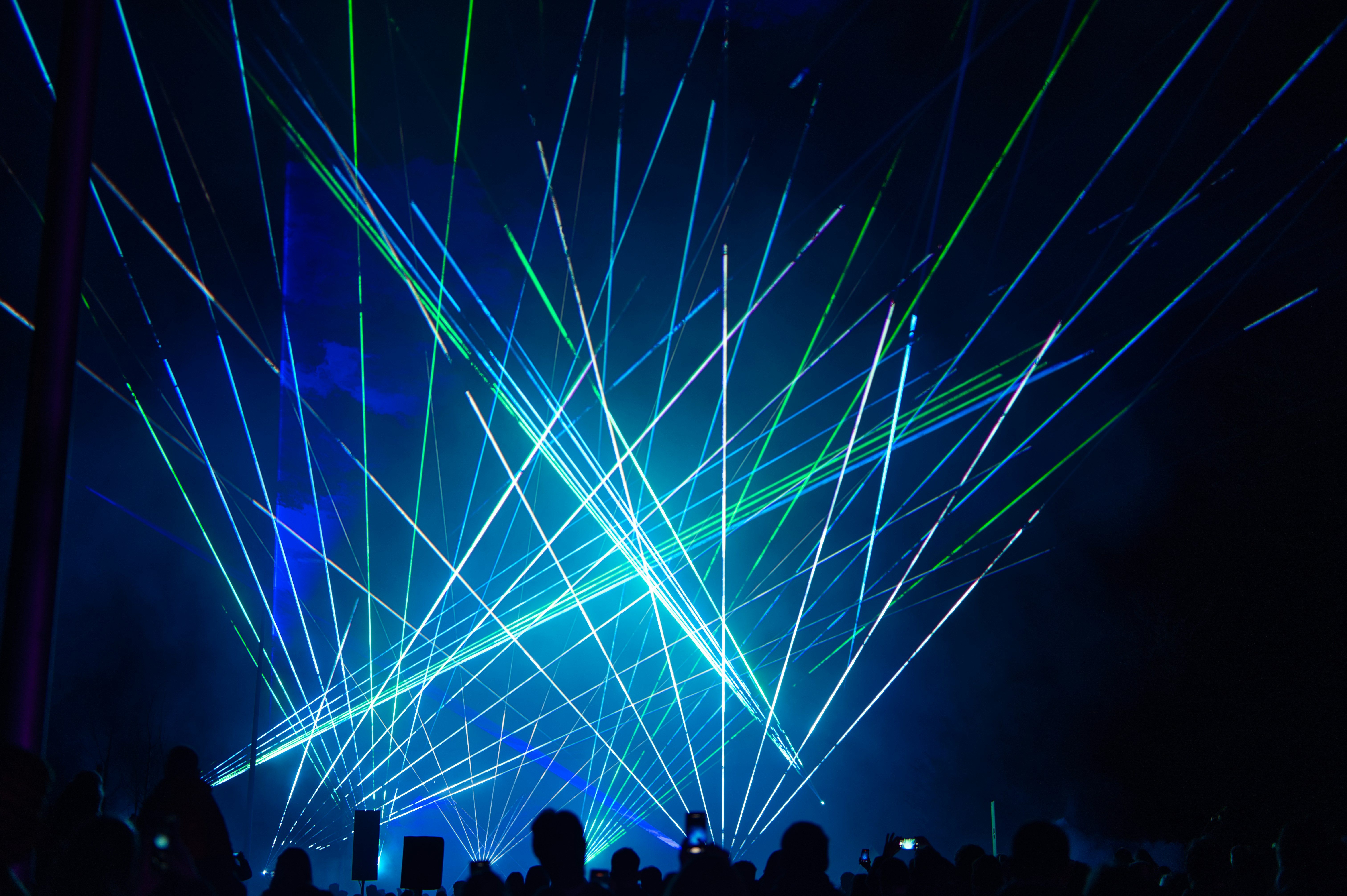 Blue and green lasers illuminate a dark concert venue.