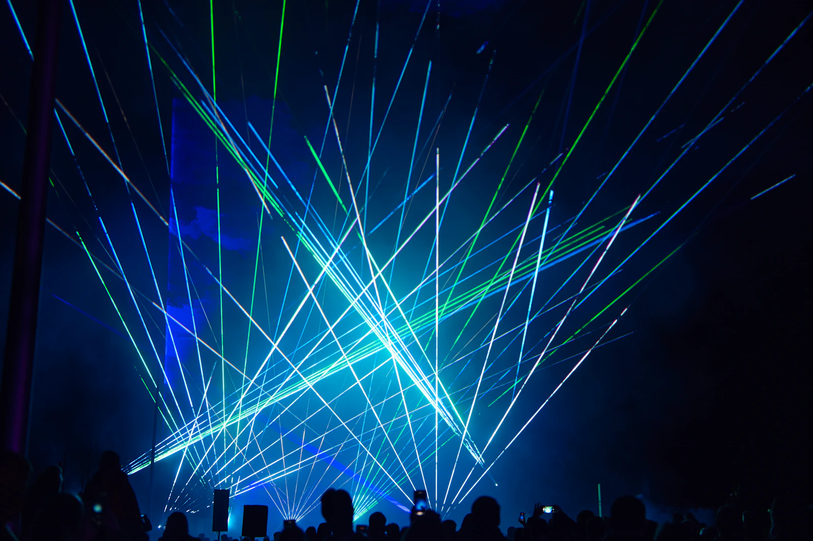 Espectáculo láser profesional con haces de luz azules y verdes sobre el público de un concierto