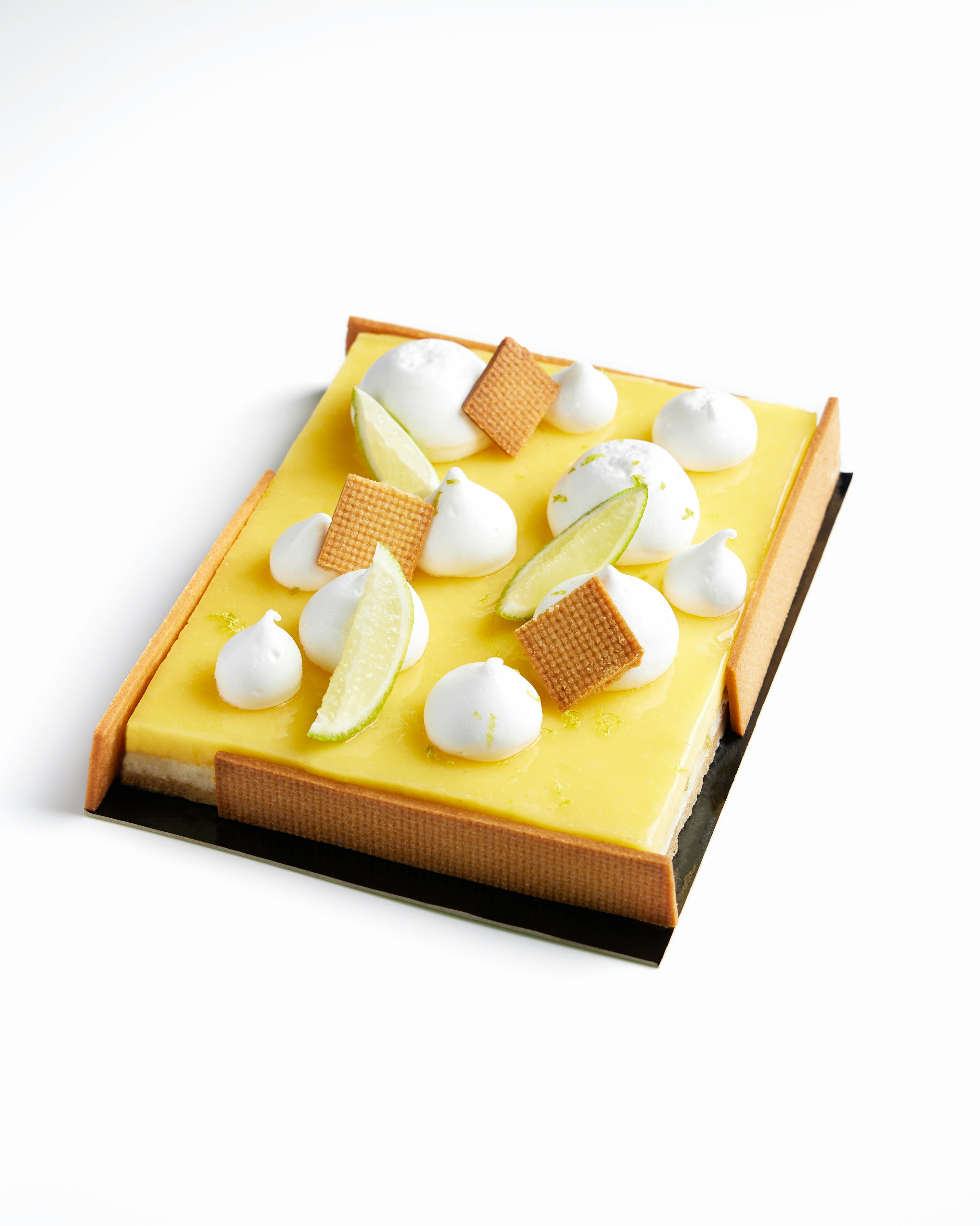 Una tarta rectangular de limón cubierta con merengue y lima.