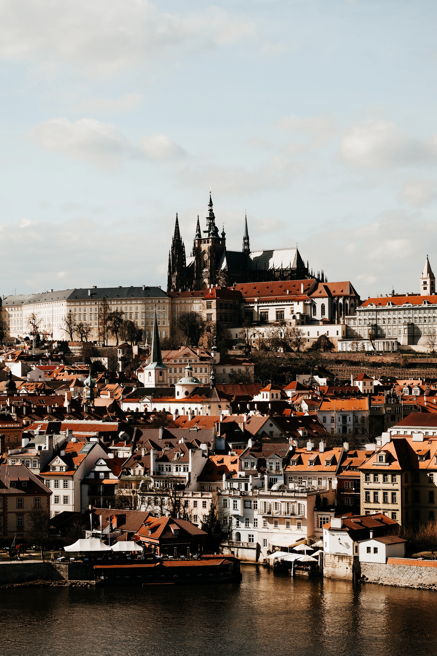 Prague Castle and St Vitus Cathedral above red rooftops beside the Vltava River