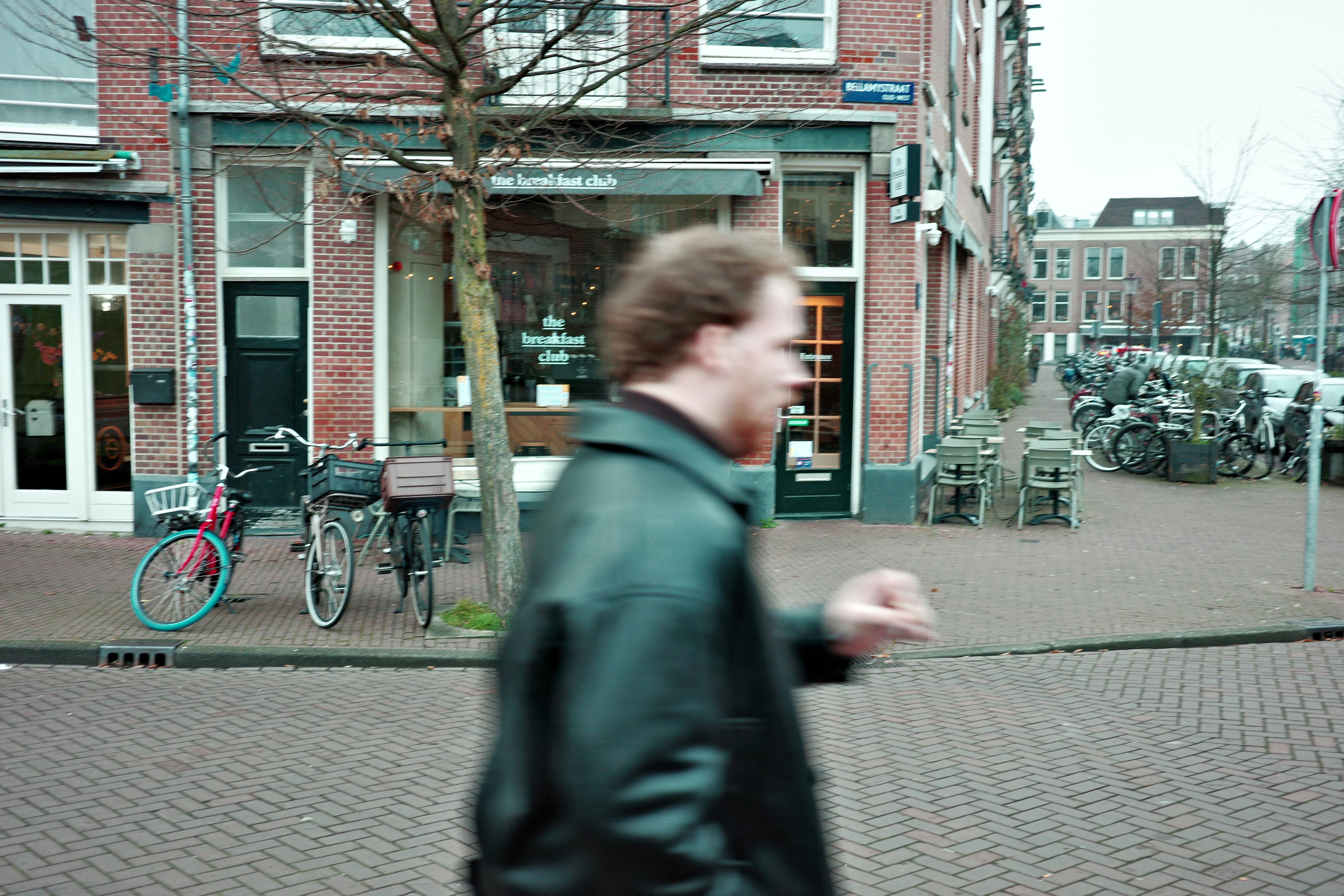 Man walking past a storefront on a brick street.