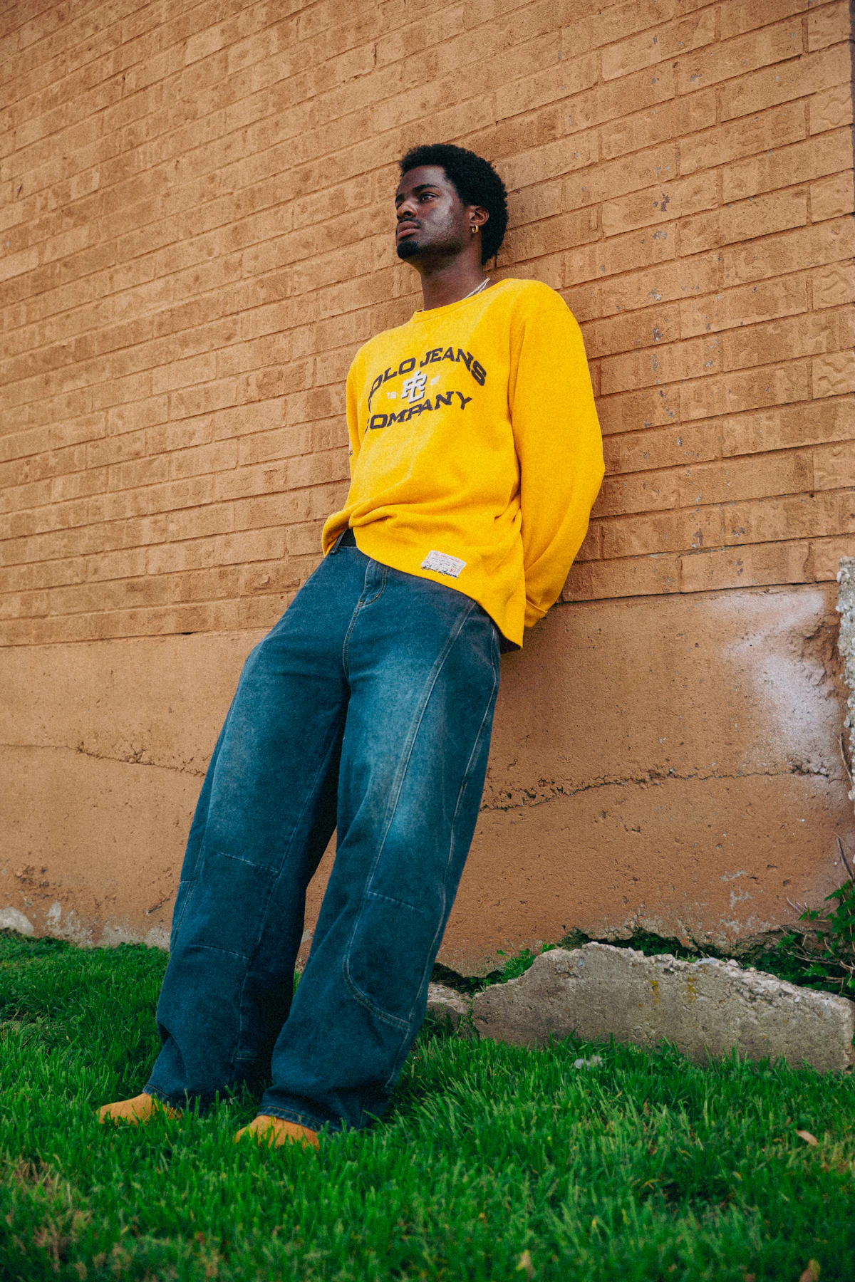 Man in a yellow heavyweight sweatshirt leaning on a brick wall