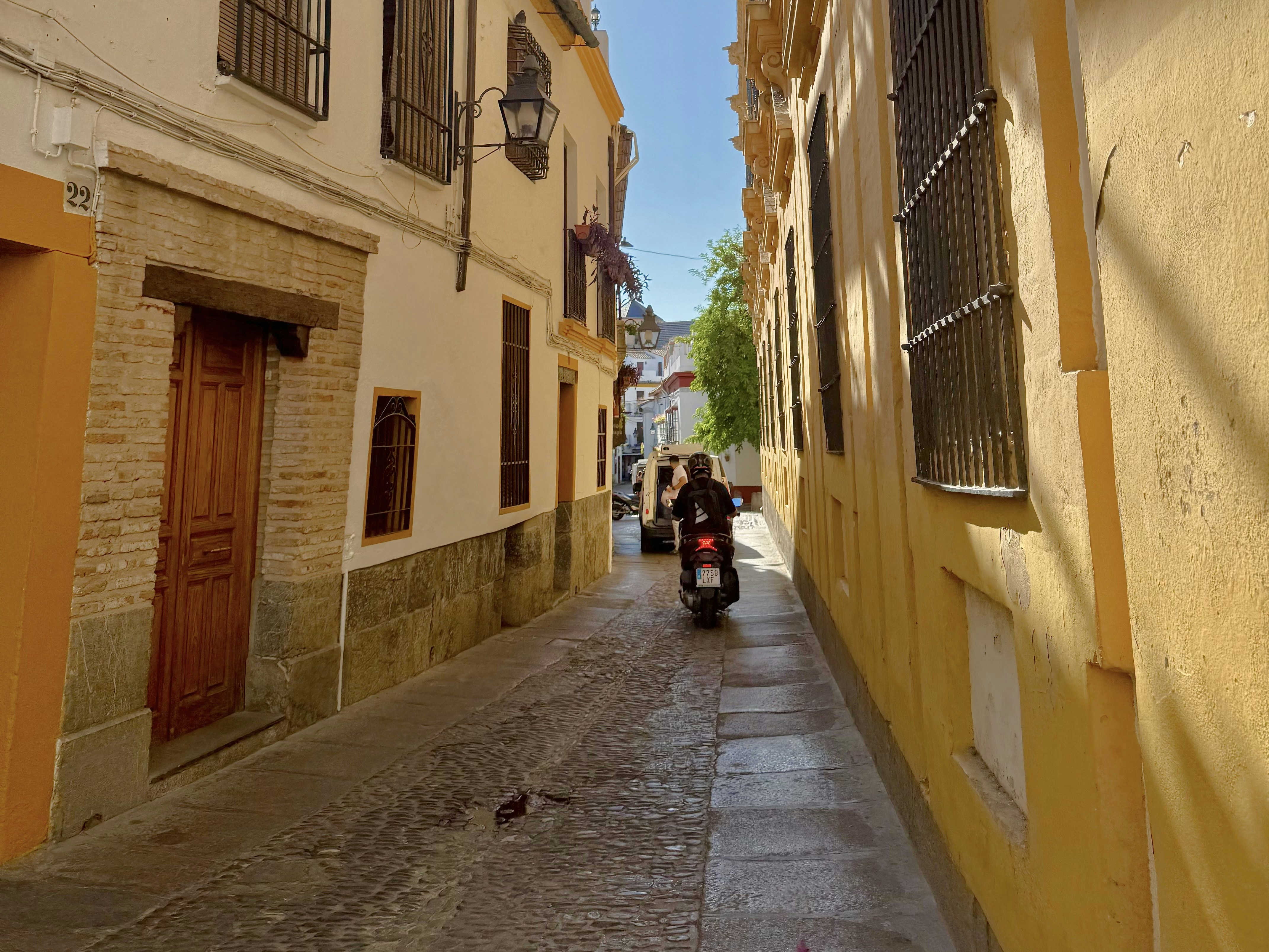 Person riding a scooter down a narrow european street.