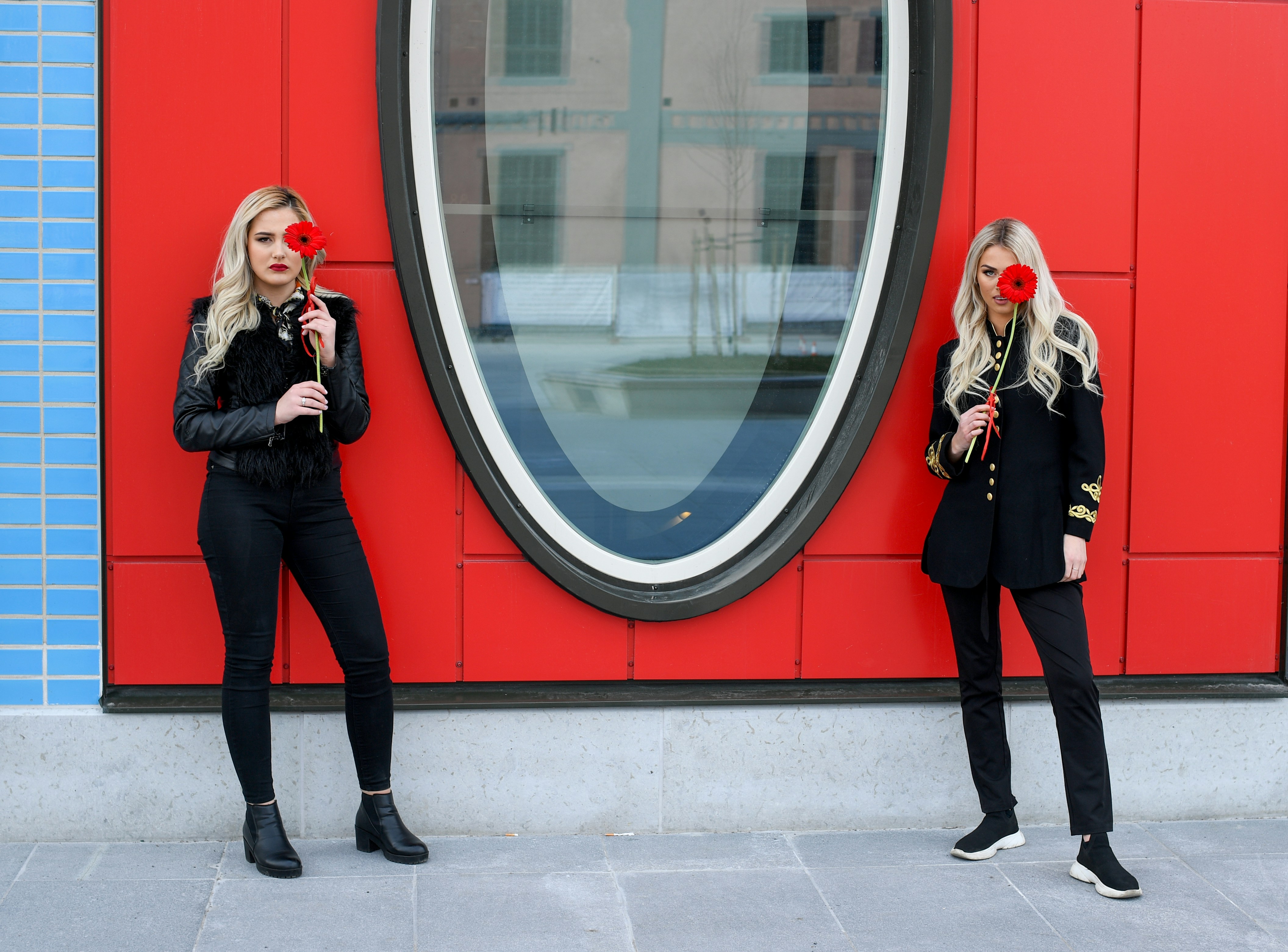 Two women in black outfits holding red roses
