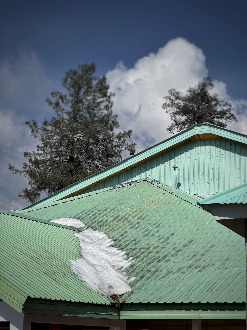 Green metal roofs with snow patches sliding off under a cloudy sky