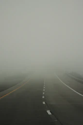 A foggy road with lane markings disappearing into mist