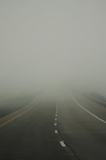 A foggy road with lane markings disappearing into mist