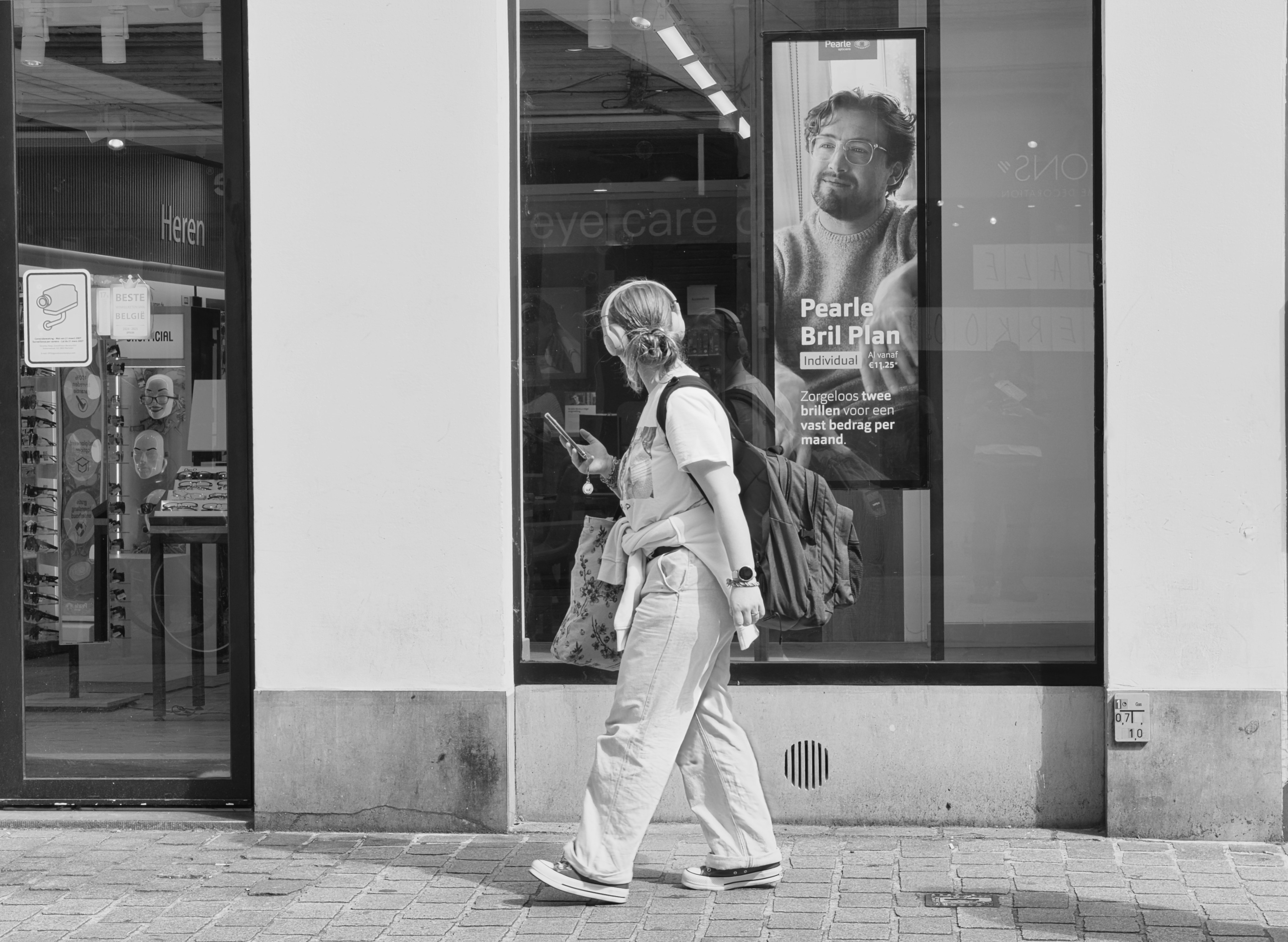 Woman wearing headphones walks past storefront with advertisement.