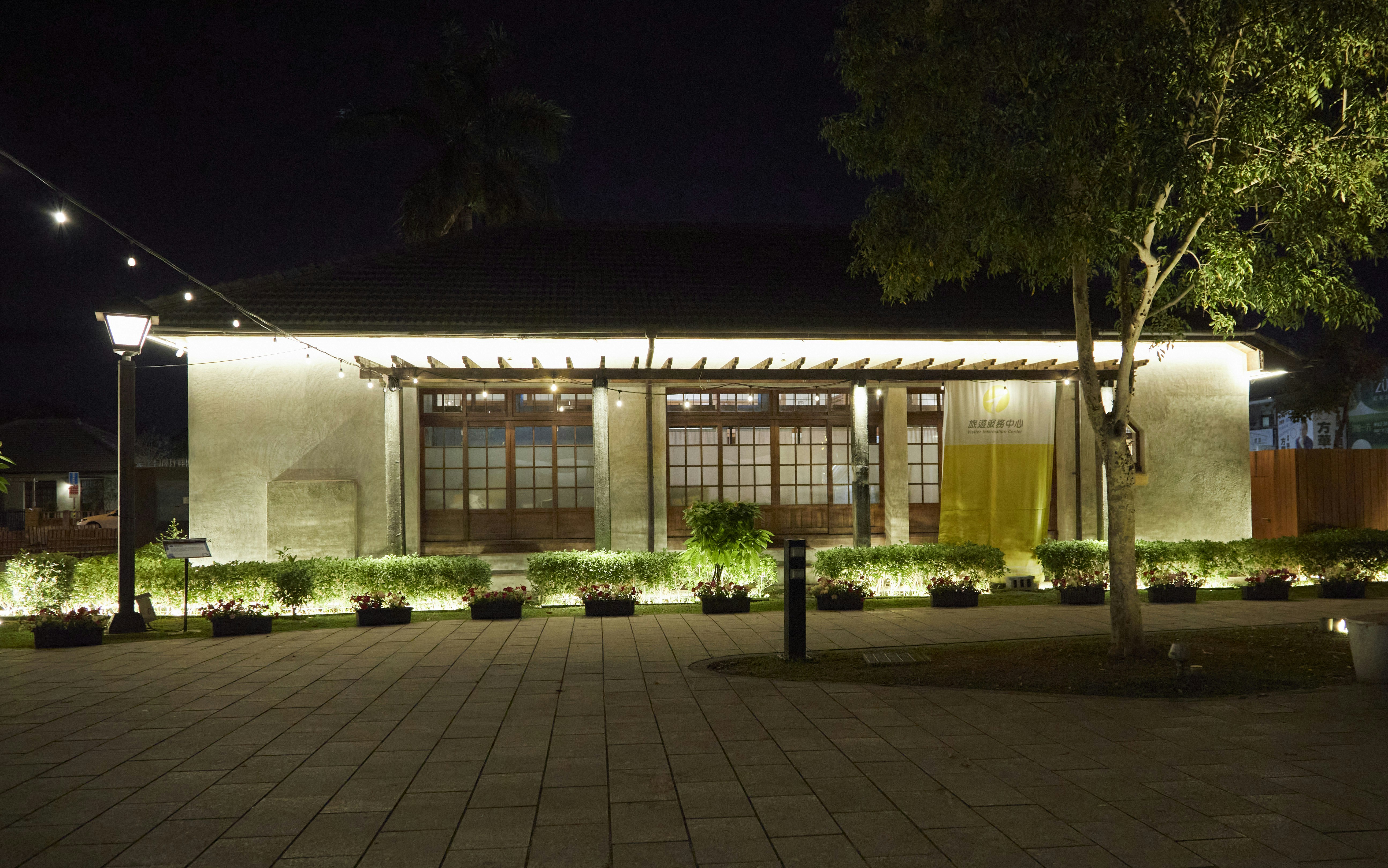 Building illuminated at night with surrounding trees and plants.