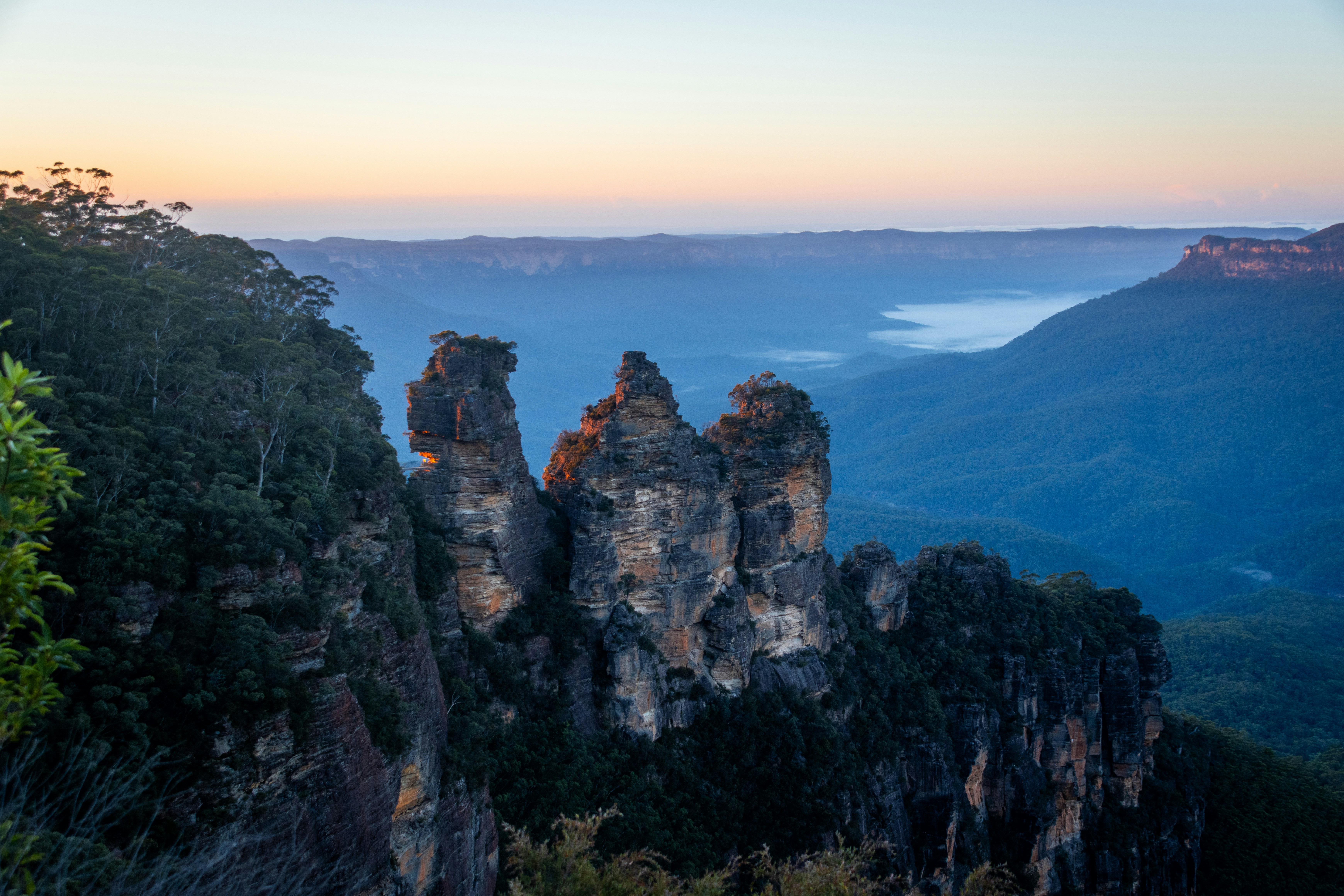 Trois formations rocheuses s’élèvent d’une vallée brumeuse à l’aube.