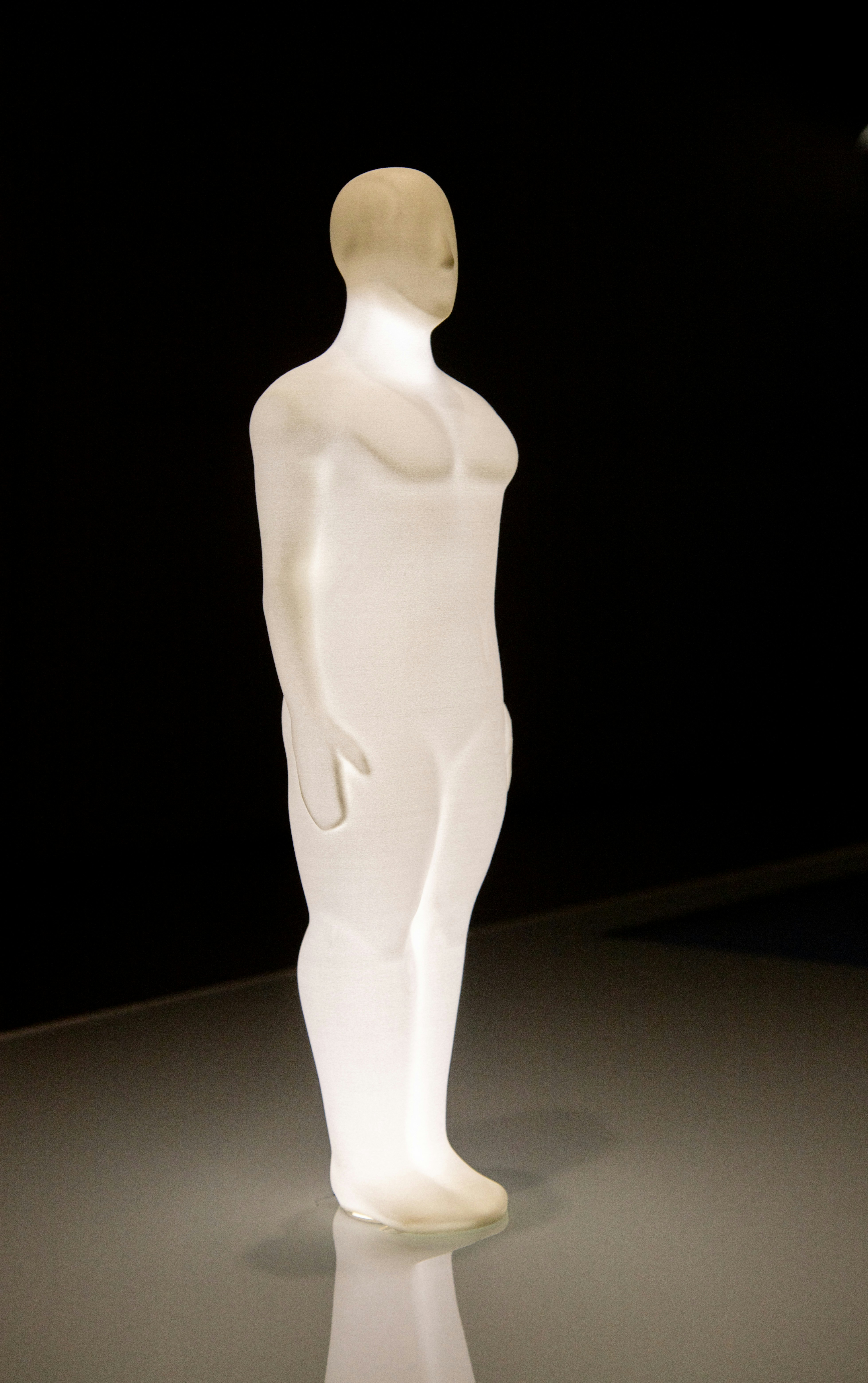 Une sculpture humaine translucide brillant sur un fond sombre.