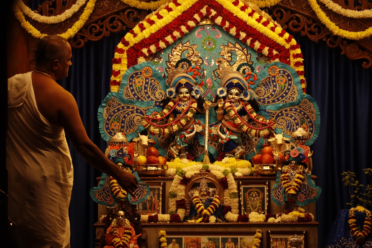 A Hindu priest in white attire offers flowers and lamp before the deities at a riverside temple