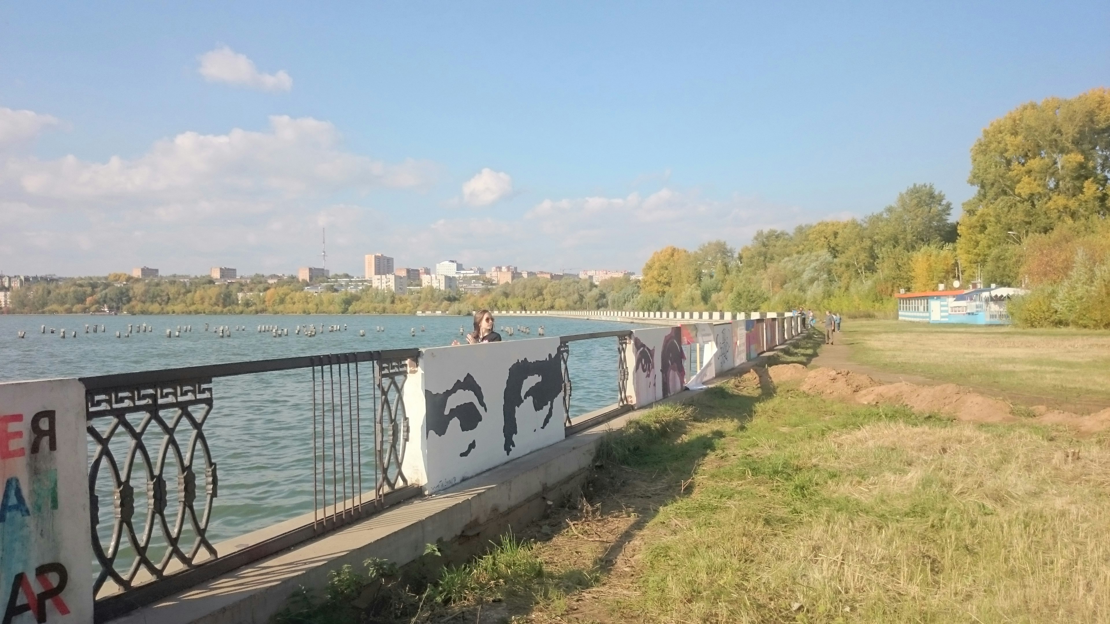 Graffiti art on a waterfront promenade with city skyline.