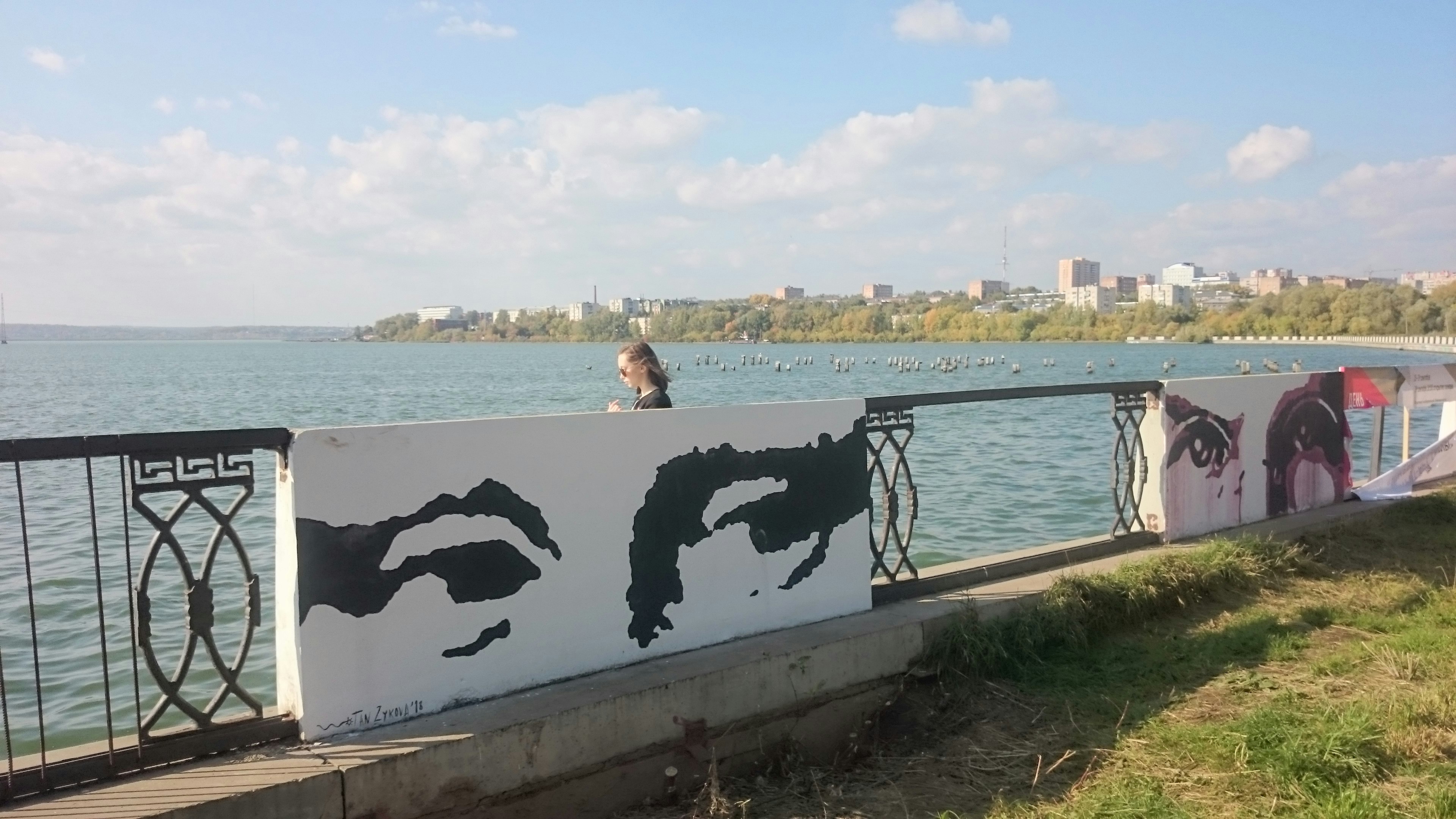 Eyes mural on a waterfront wall with city skyline.